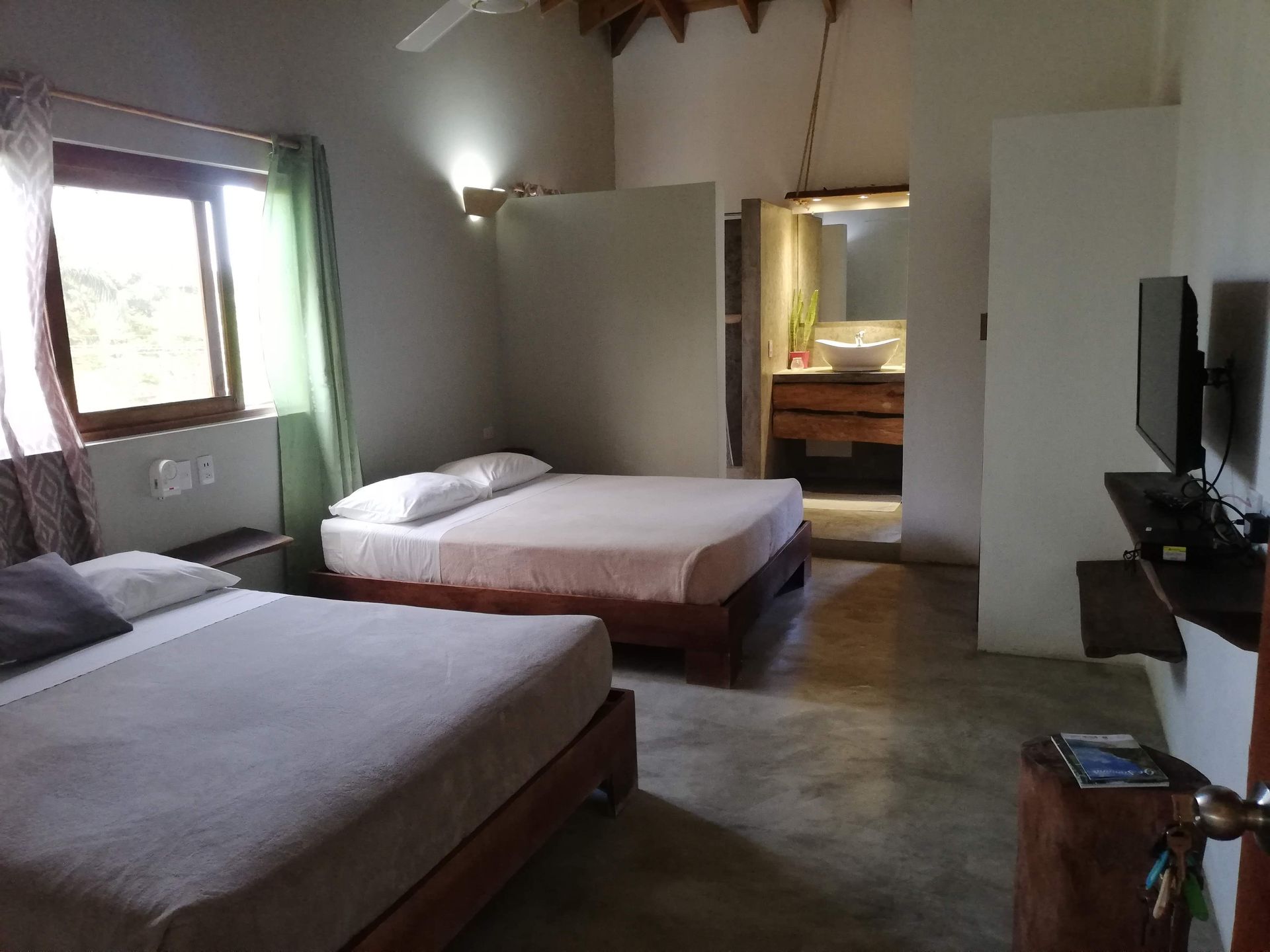 Bedroom with two beds, window, open bathroom. White walls, grey bedding, wooden furniture.