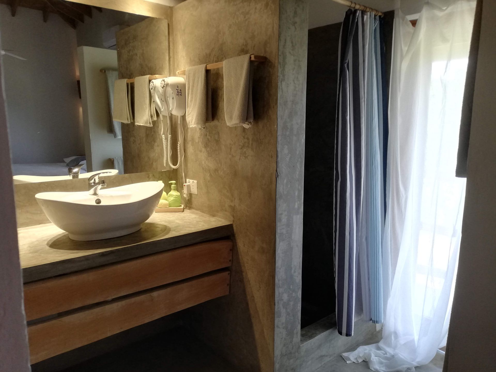 Bathroom with a concrete sink, wooden drawers, towels, and a shower with blue and white curtains.
