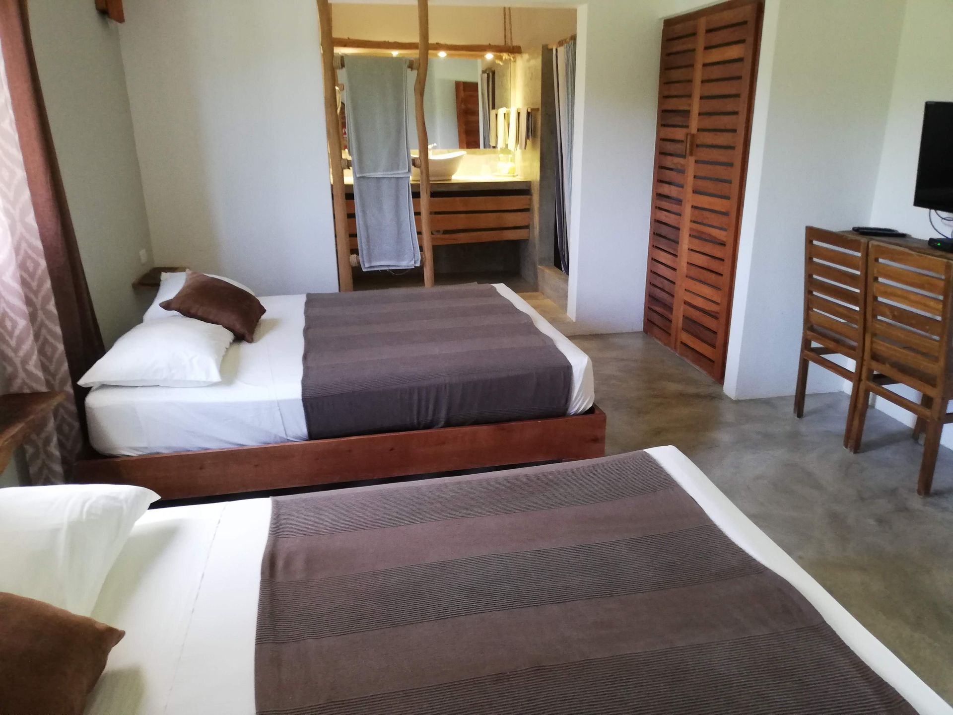 Two beds with brown blankets in a room, bathroom visible in the background, wooden furniture.