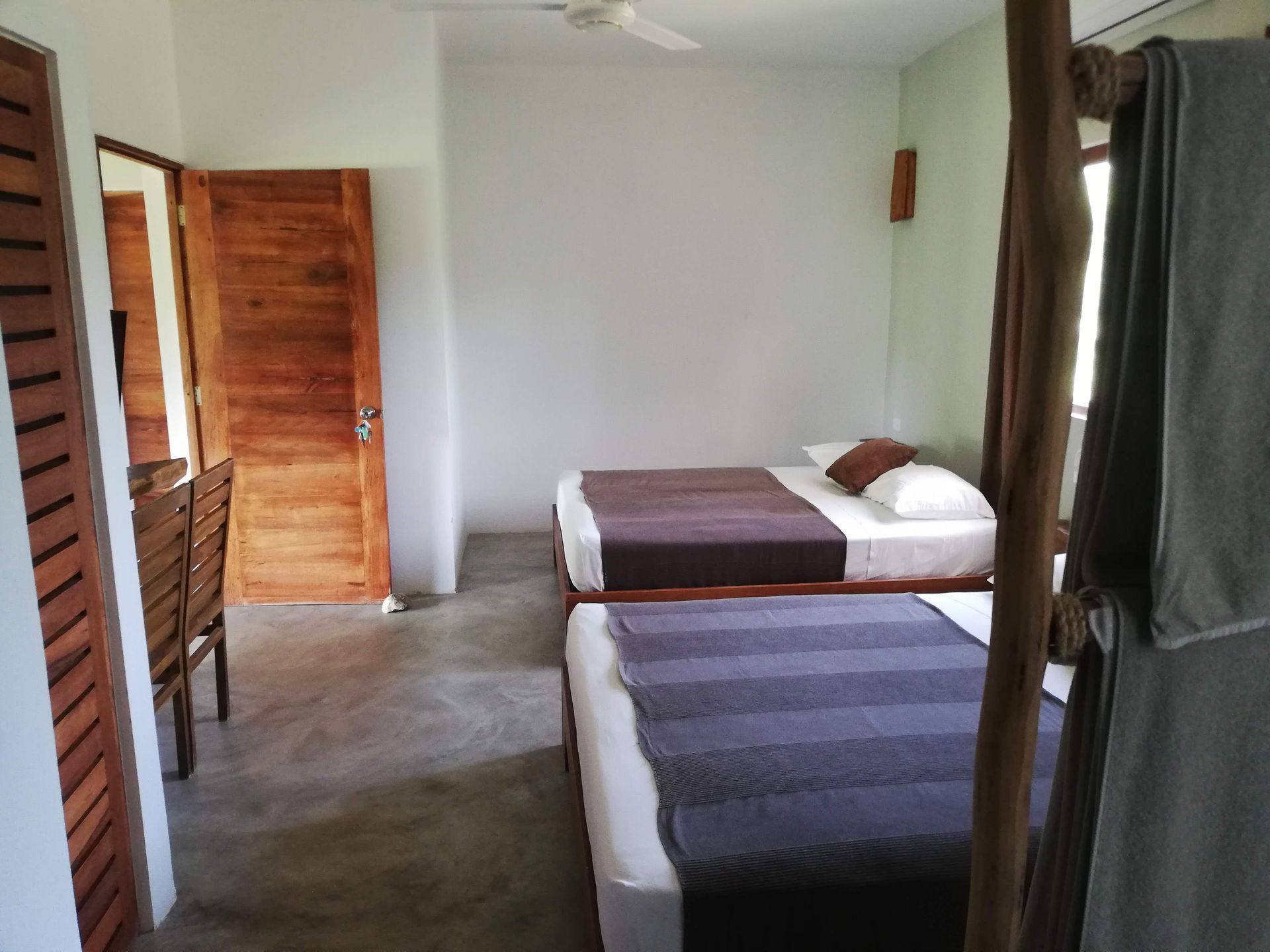 Bedroom with two beds, wooden door and furniture, white walls, and a towel on a wooden rack.