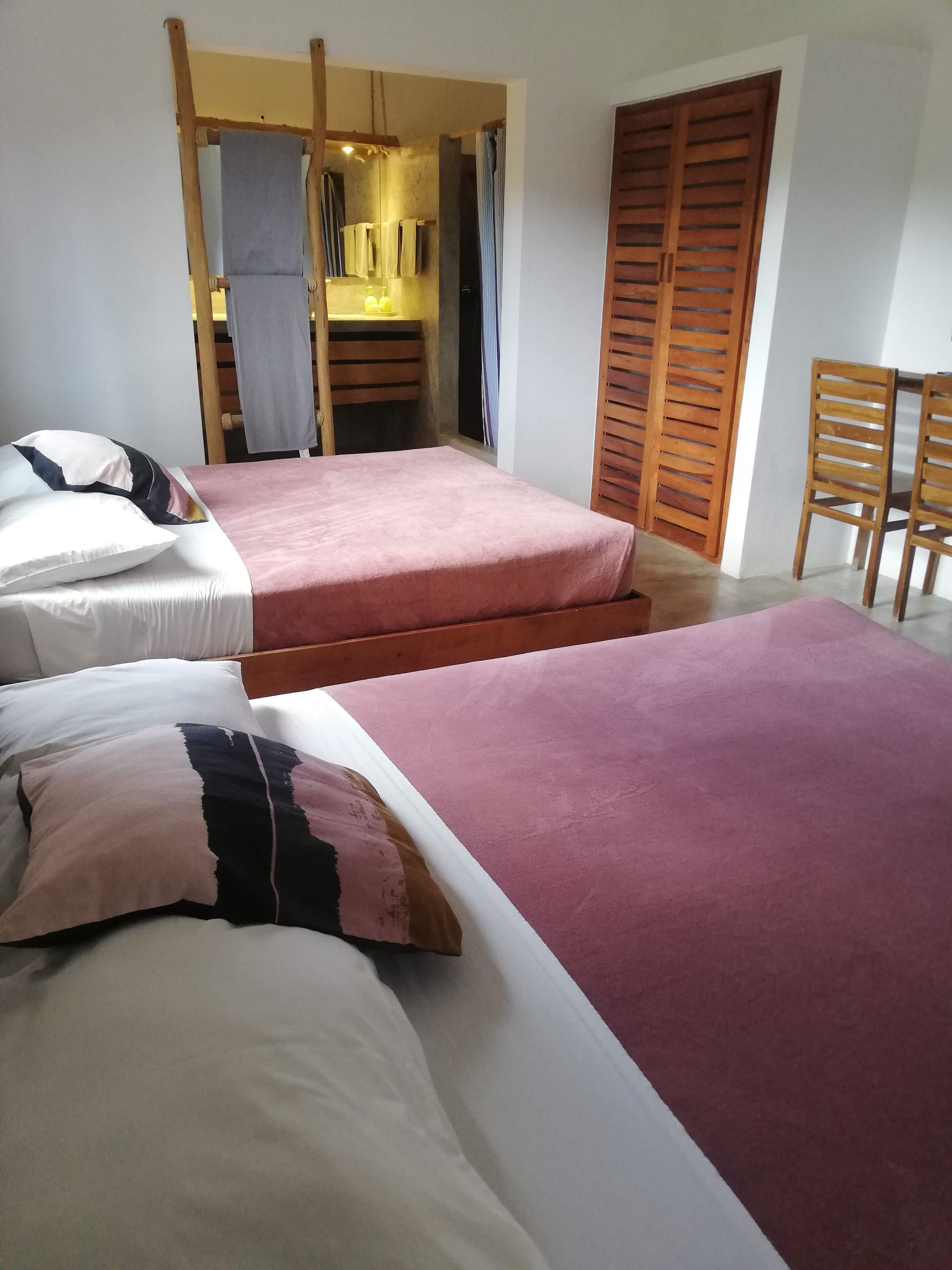 Bedroom with three beds; two pink, one white. Bathroom visible through doorway.