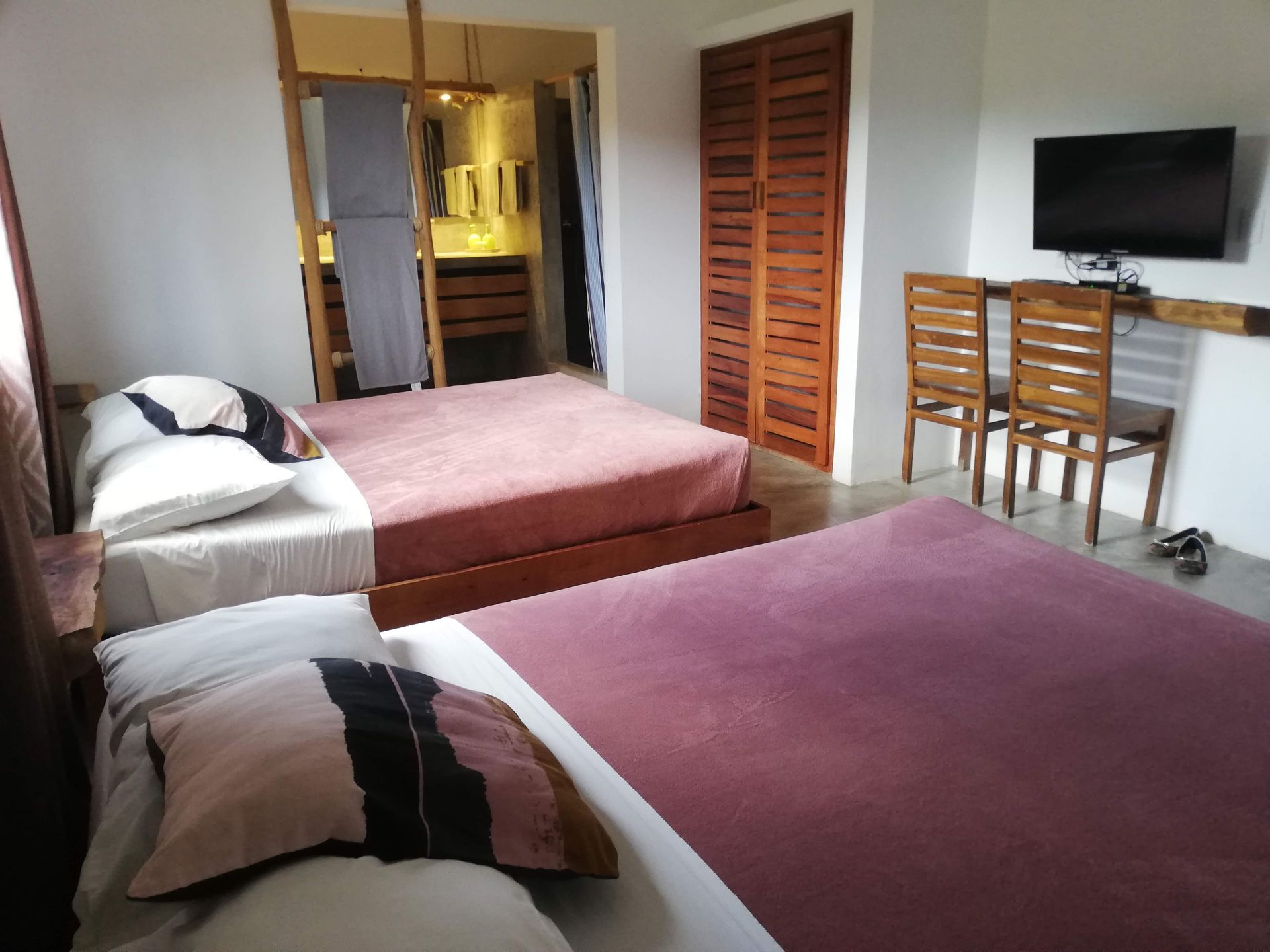 Bedroom with two beds, wooden furniture, and a TV. Pink and white bedding.