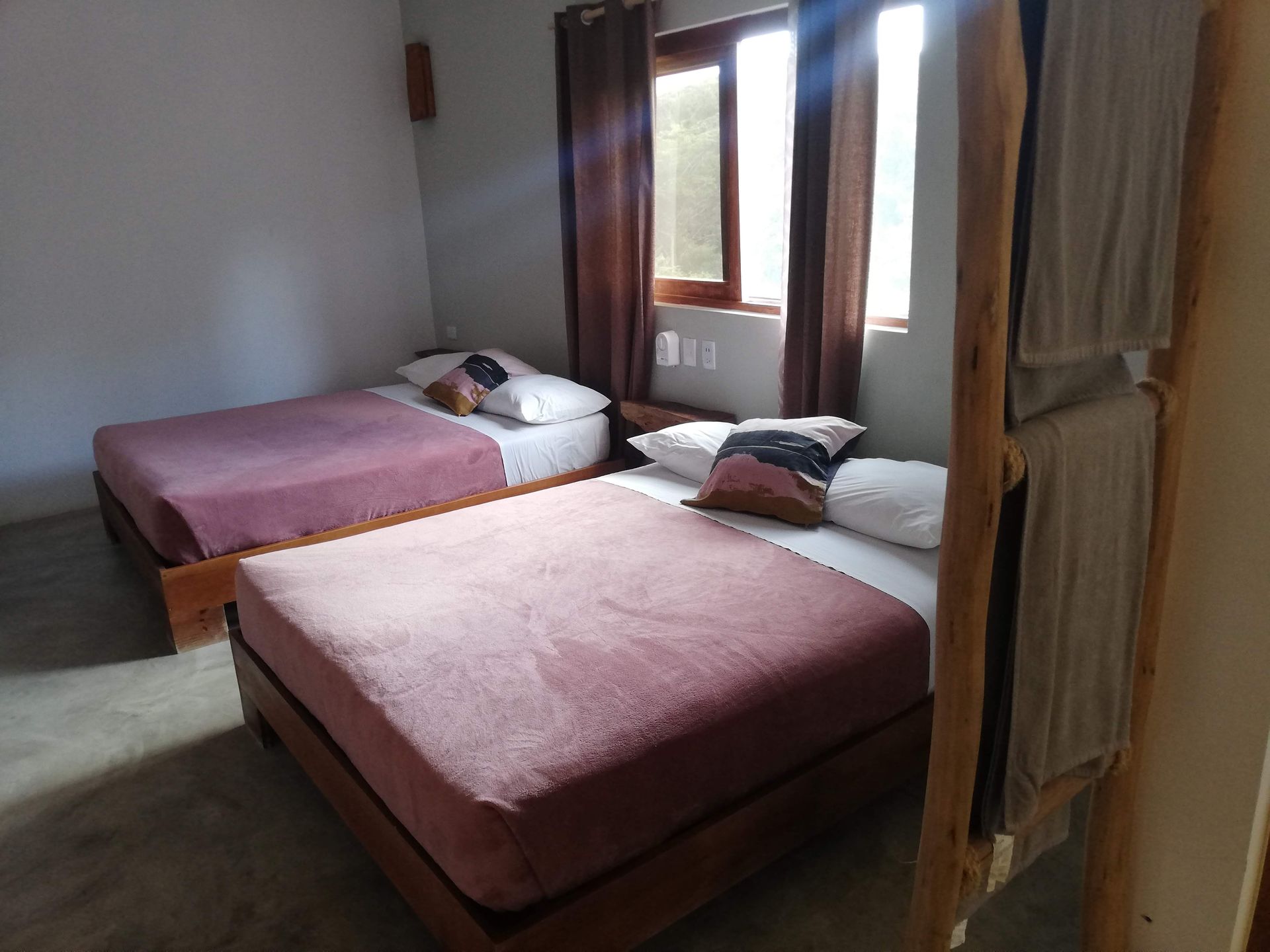 Two beds in a room, one double, one twin, near a window with brown curtains.