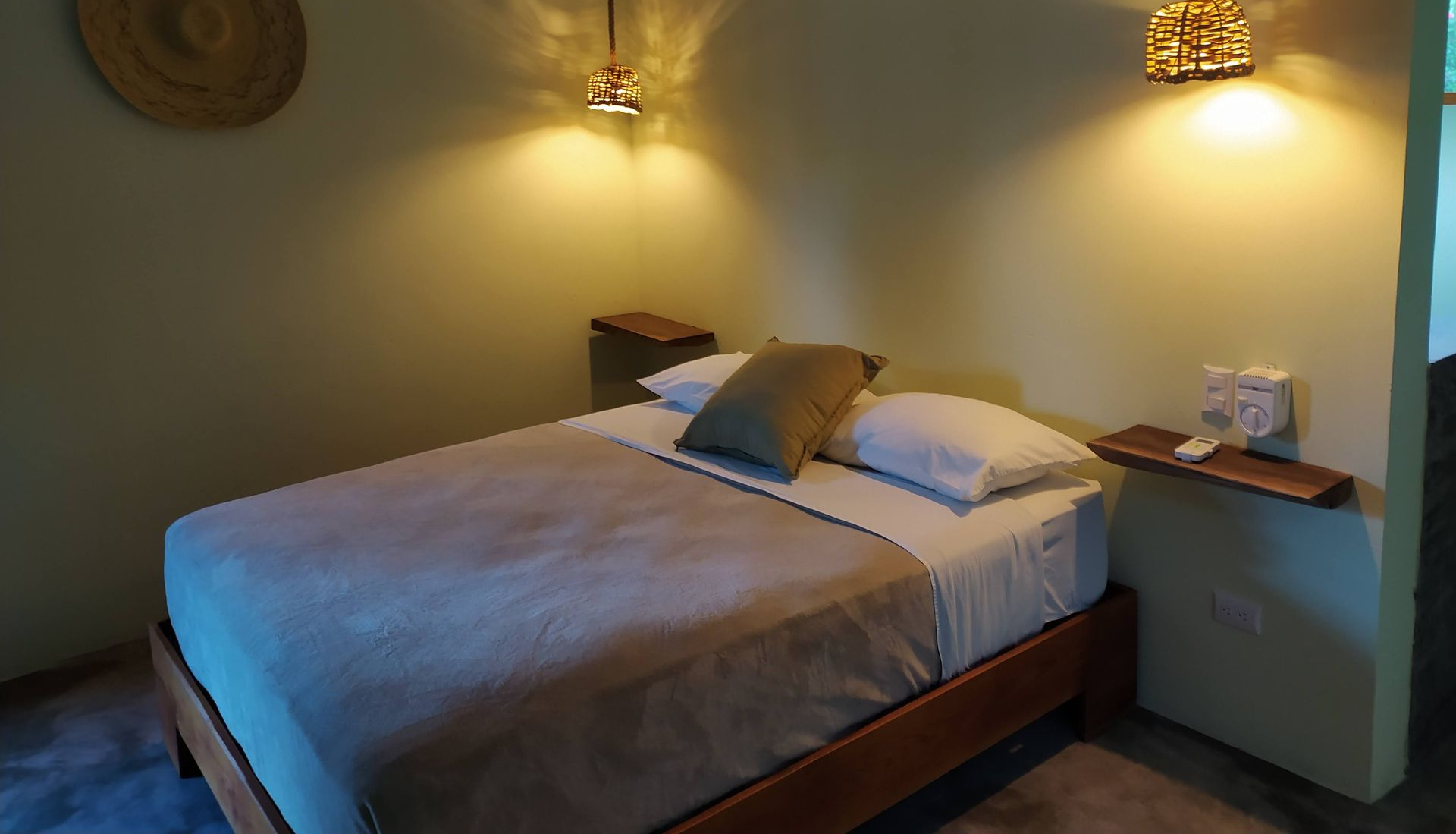 Bedroom with a bed, two pendant lights, and decorative items. Pale green walls.