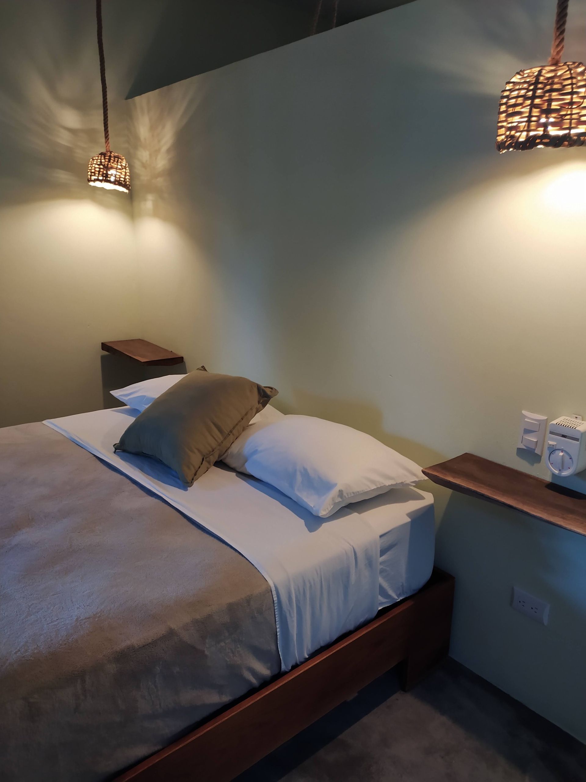Bedroom with a bed, two lamps, and small tables; light green walls.