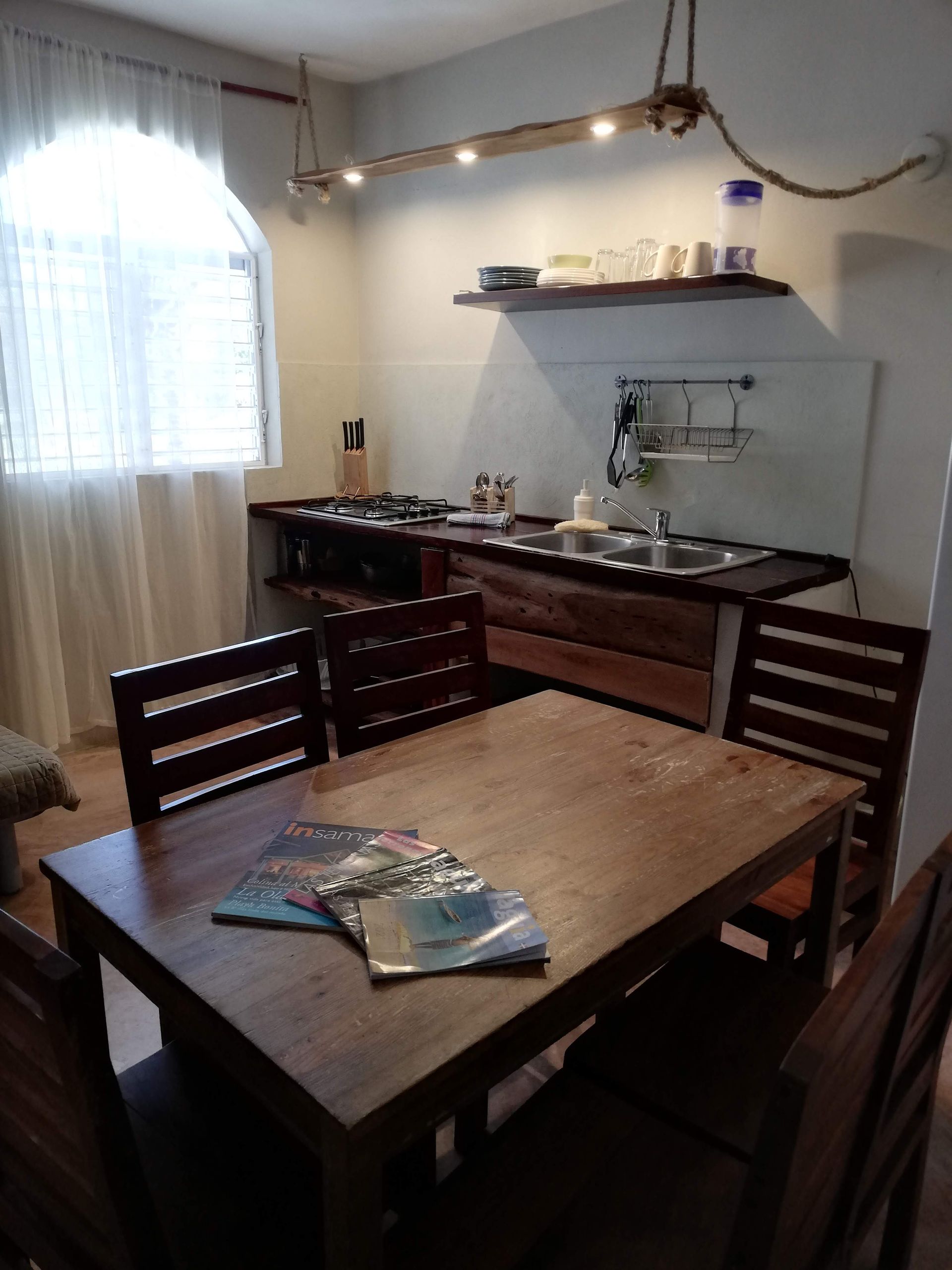 Kitchen and dining area with wooden table, chairs, and stove; shelf with dishes.