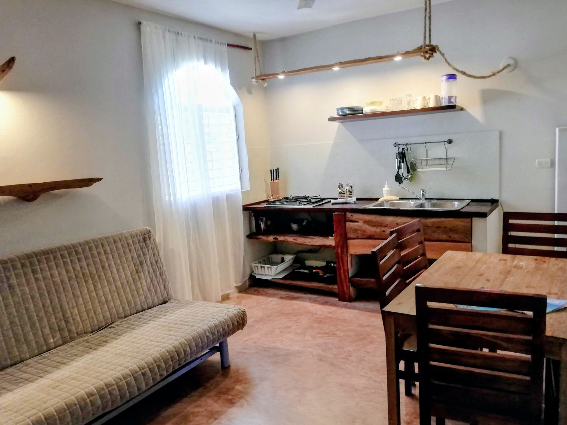 Cozy kitchen and dining area with rustic wood accents and a futon. Bright light streams in from a sheer curtained window.