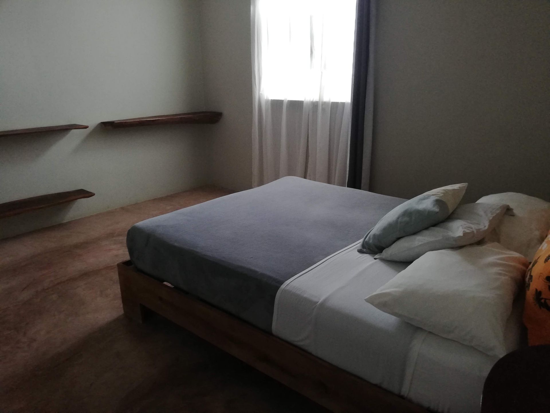 Bedroom with bed, pillows, window, floating shelves, and wooden floor.