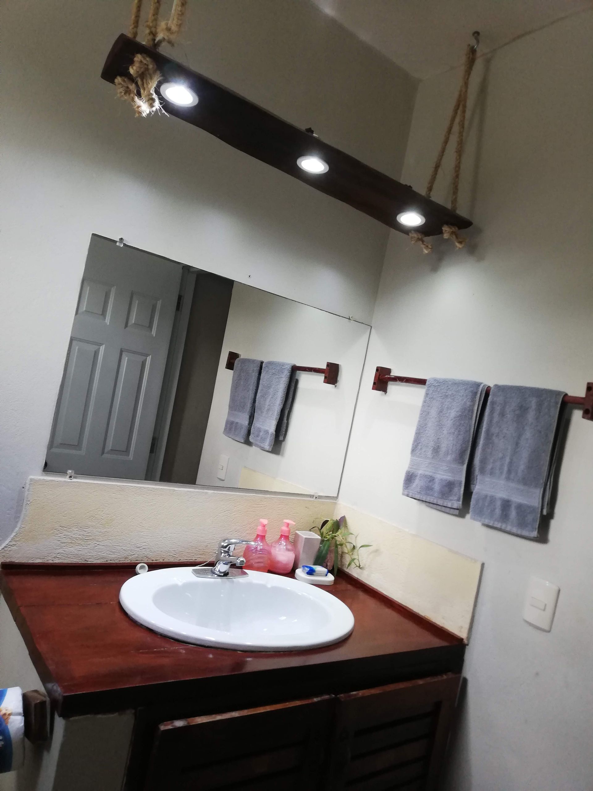 Bathroom vanity with mirror, sink, towel racks, and hanging light fixture. Dark wood, gray towels, and white sink.