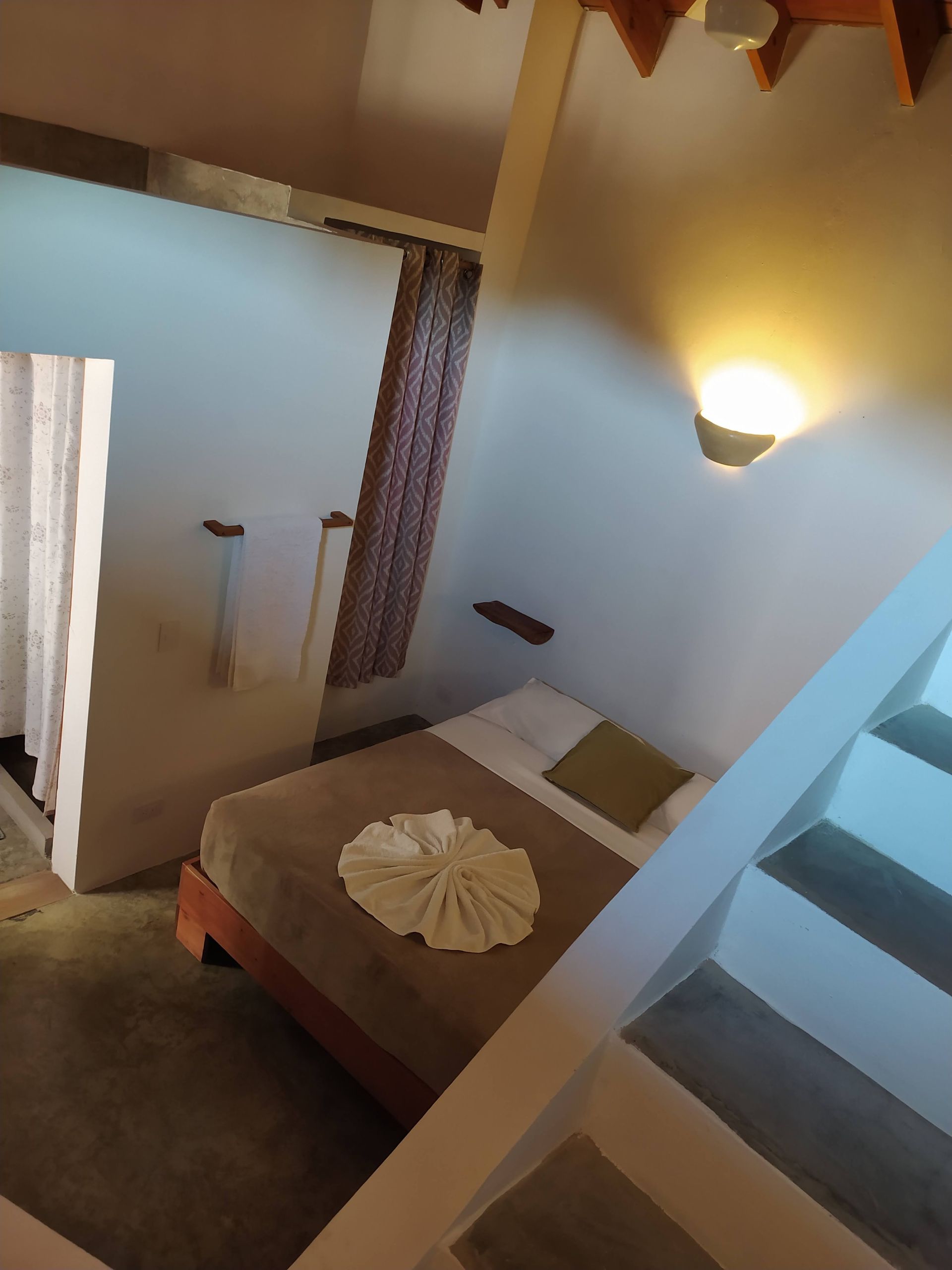 Small, bright bedroom with bed, white folded towel, and a small stairway.