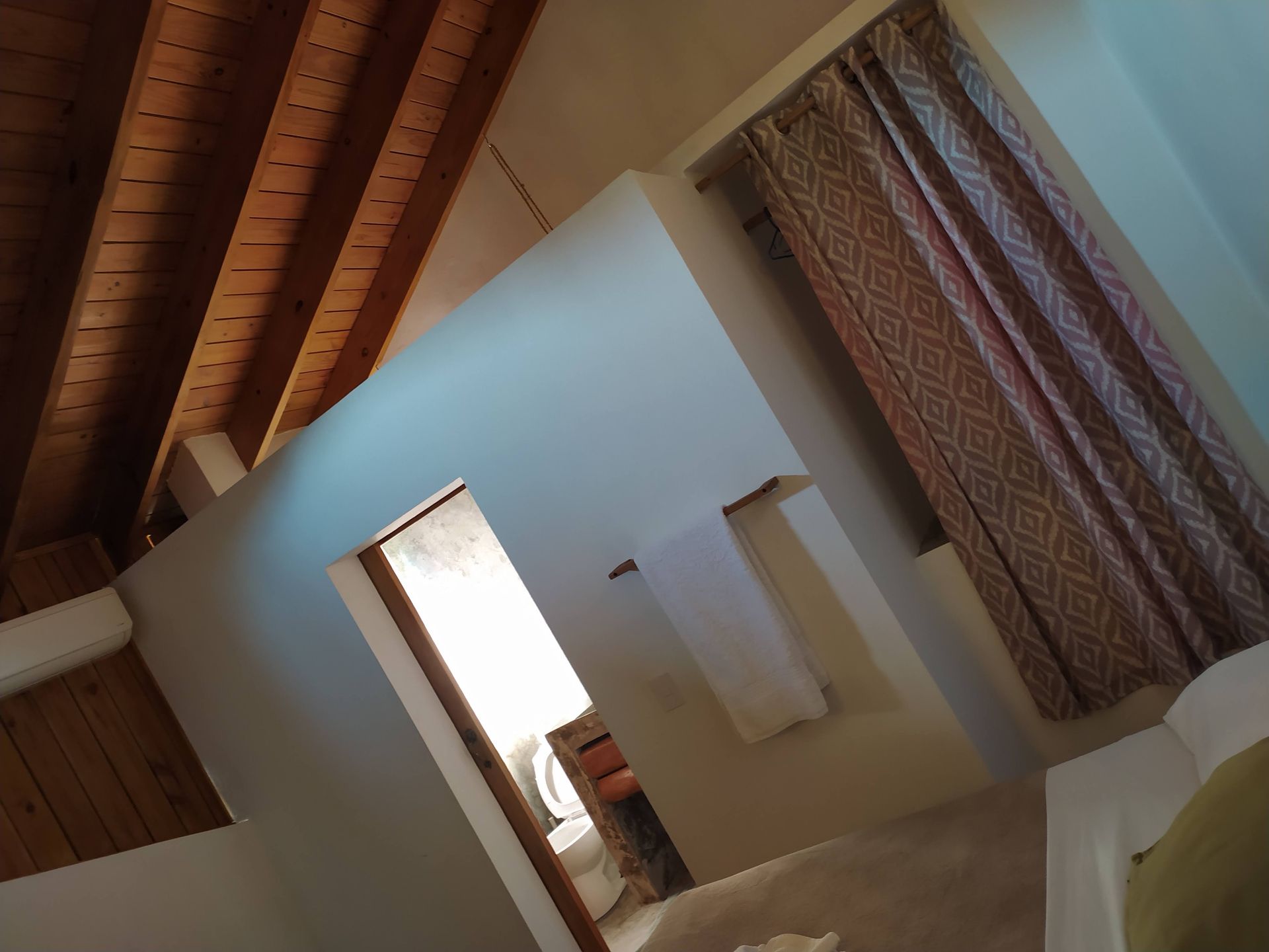 Interior view of a room with wooden beams and a doorway. Brown patterned curtains hang on the right.