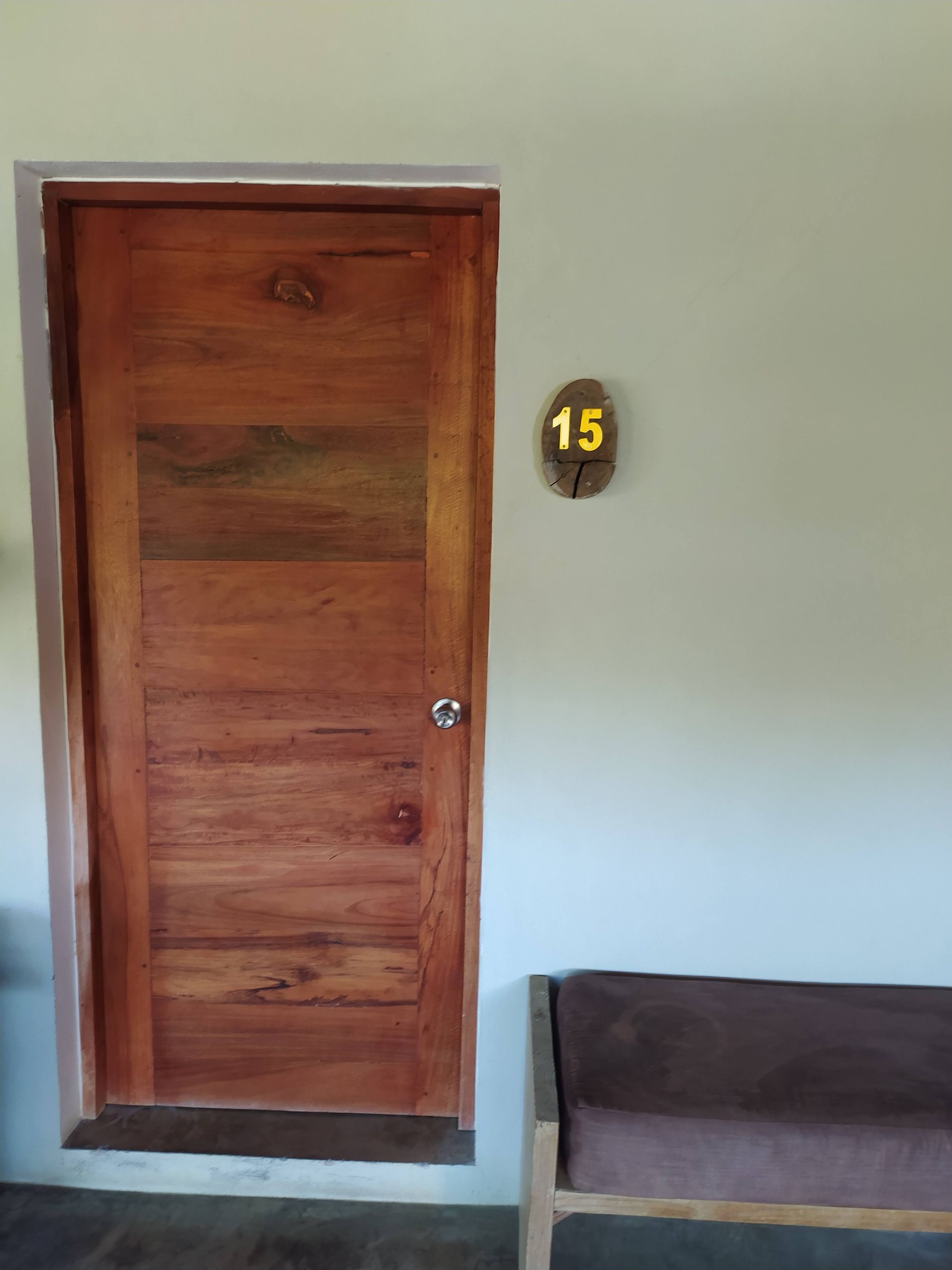 Wooden door with room number 15 and a bench next to it, set against a light-colored wall.