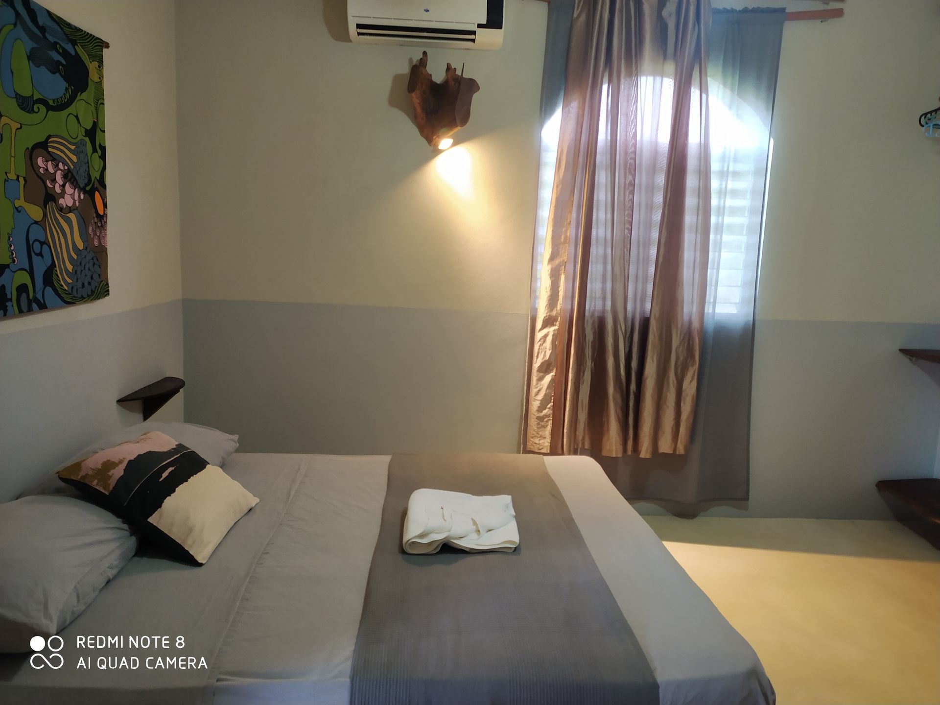 Bedroom with bed, art, window with curtains, air conditioner, and wall decor.