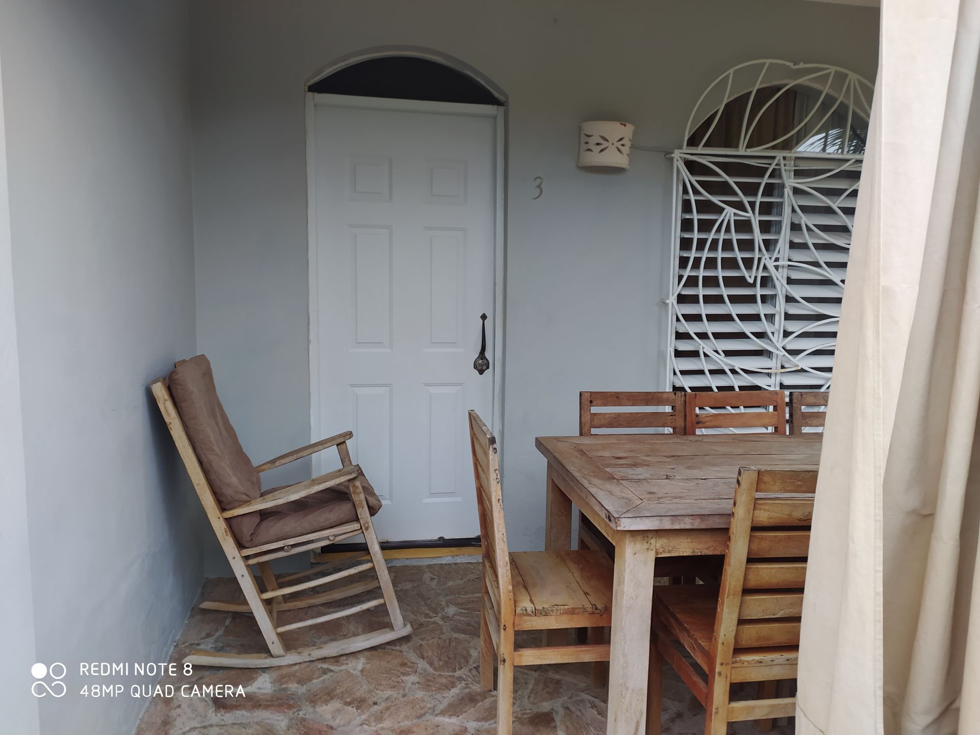 A patio with a white door, rocking chair, wooden table, and chairs.