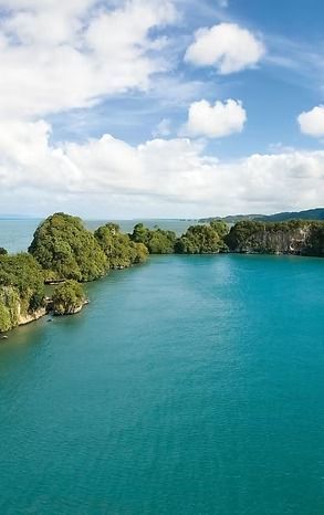 Emerald green islands in turquoise water under a blue sky with fluffy white clouds.
