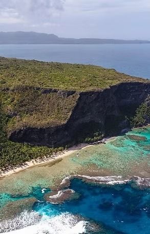 Aerial view of tropical coast with turquoise water, a sandy beach, and a cliff covered in greenery.