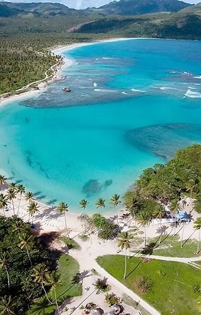 Aerial view of a turquoise bay with white sand beach and lush green palm trees.