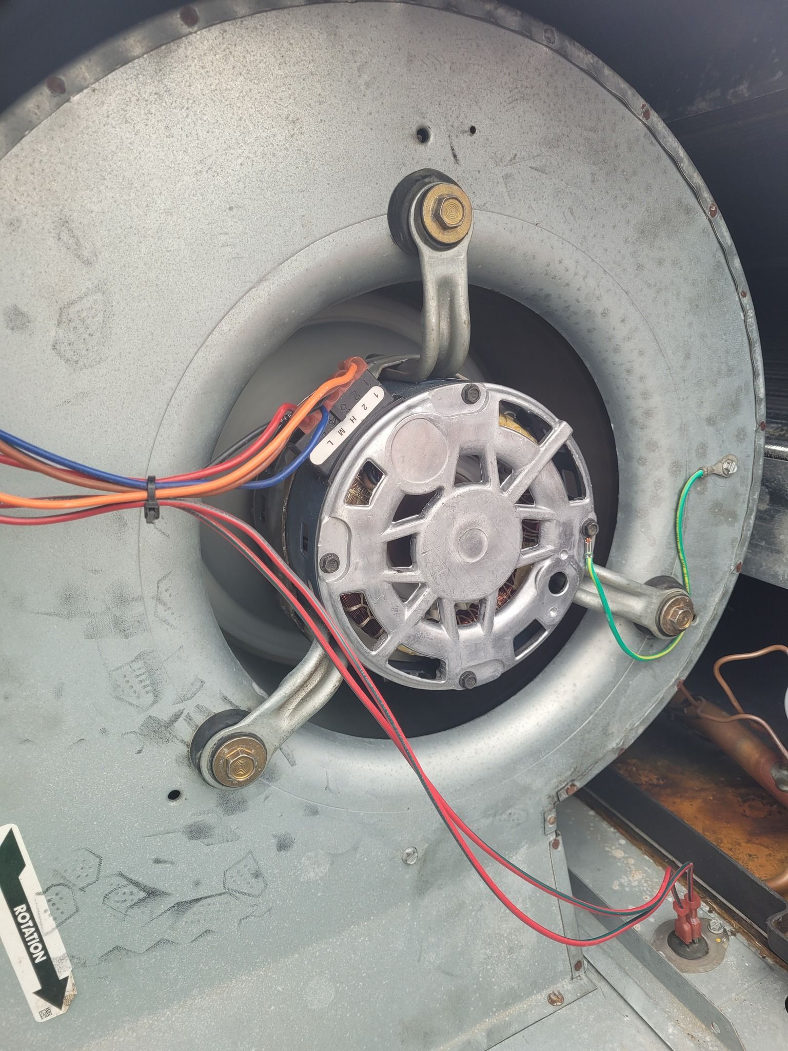 A blower motor mounted inside a metal HVAC fan housing, featuring colorful wiring and a green grounding wire.