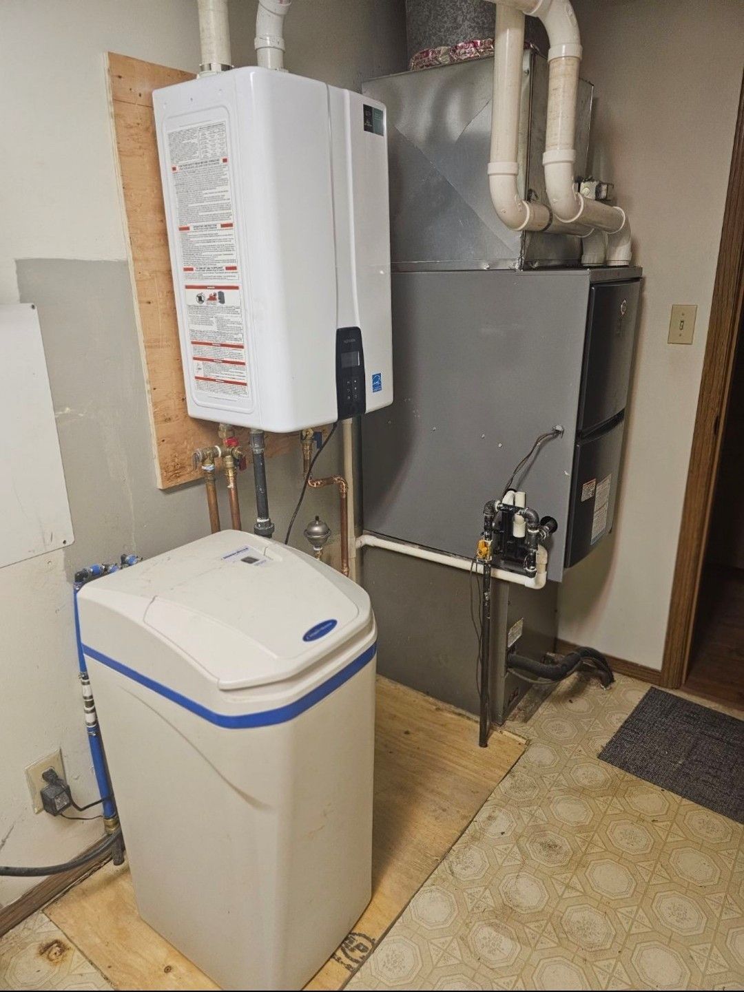 A white tankless water heater, a grey furnace, and a water softener installed in a residential utility room.