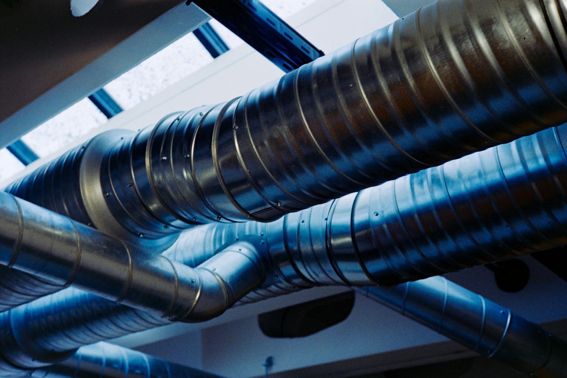 Blue metallic ventilation ducts crossing a ceiling in an industrial interior