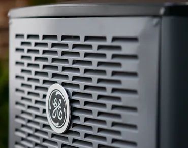 Close-up of a grey GE air conditioner unit with a branded circular logo on its vented metal panel.