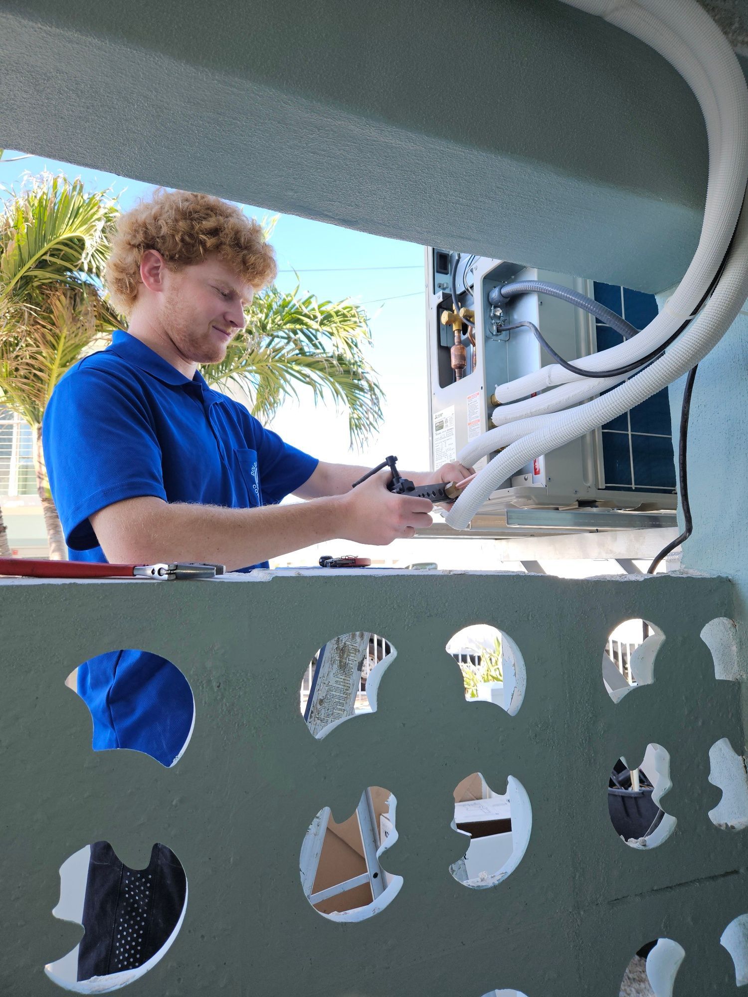 HVAC technician with curly hair installs air conditioning unit on a building exterior.