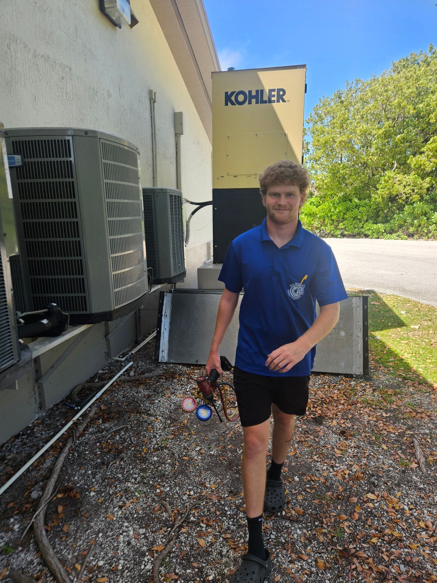 Man in blue shirt and black shorts walks past AC units and a Kohler generator.