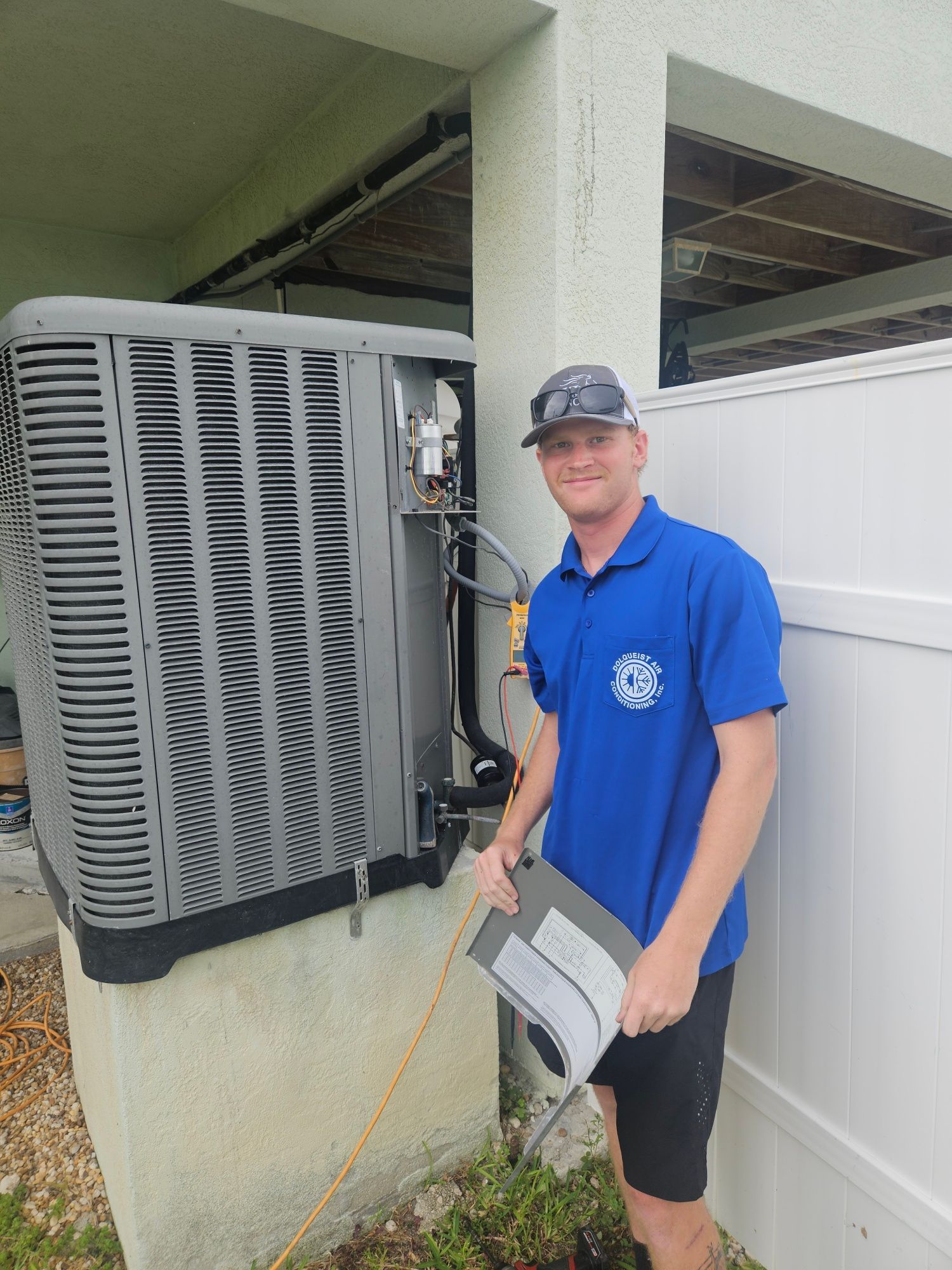 Man in blue shirt with clipboard inspecting HVAC unit outdoors.