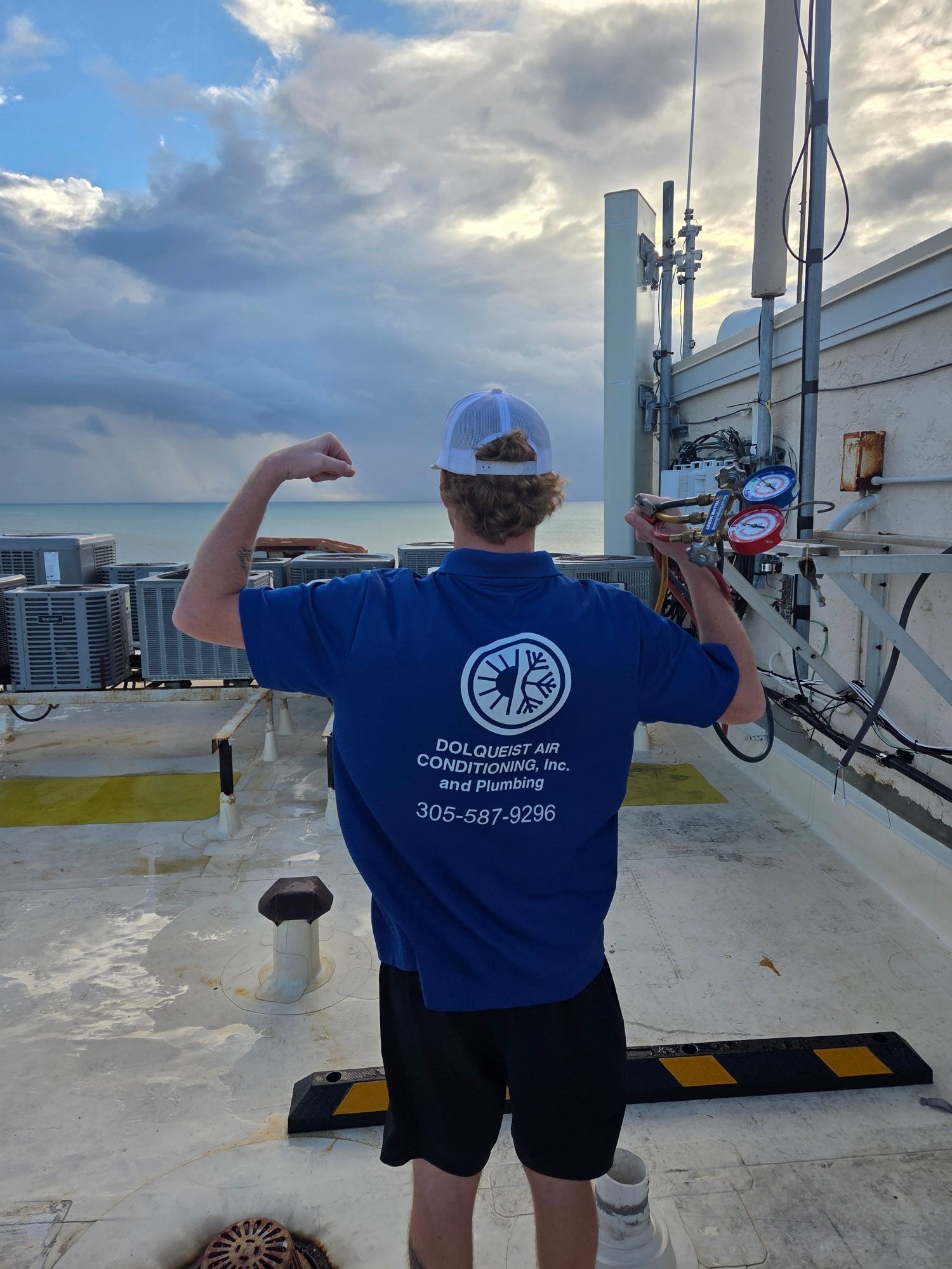 Person flexing on a rooftop, wearing a blue polo shirt with a logo, holding gauges.