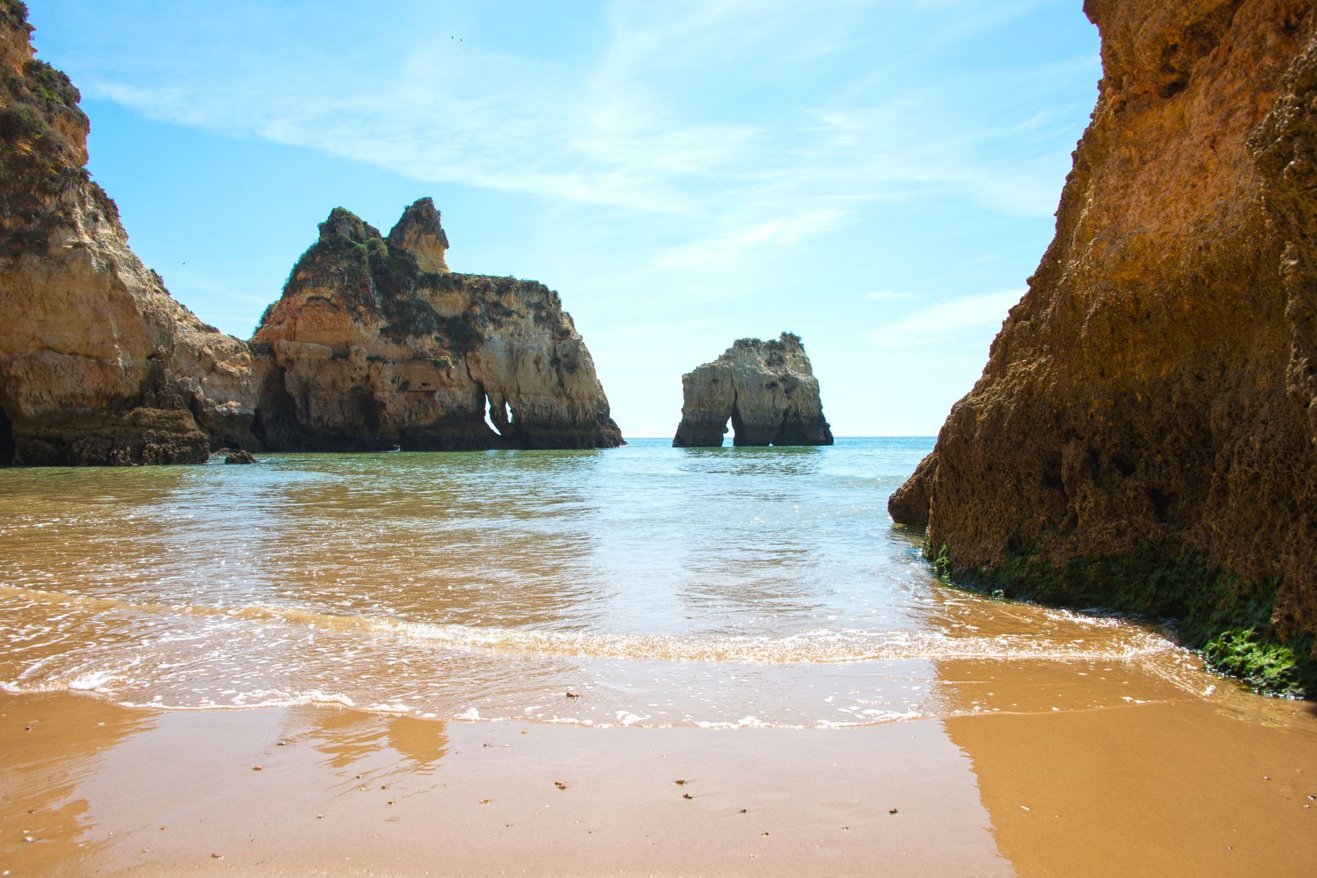 Sandy beach with ocean and rock formations against a blue sky.