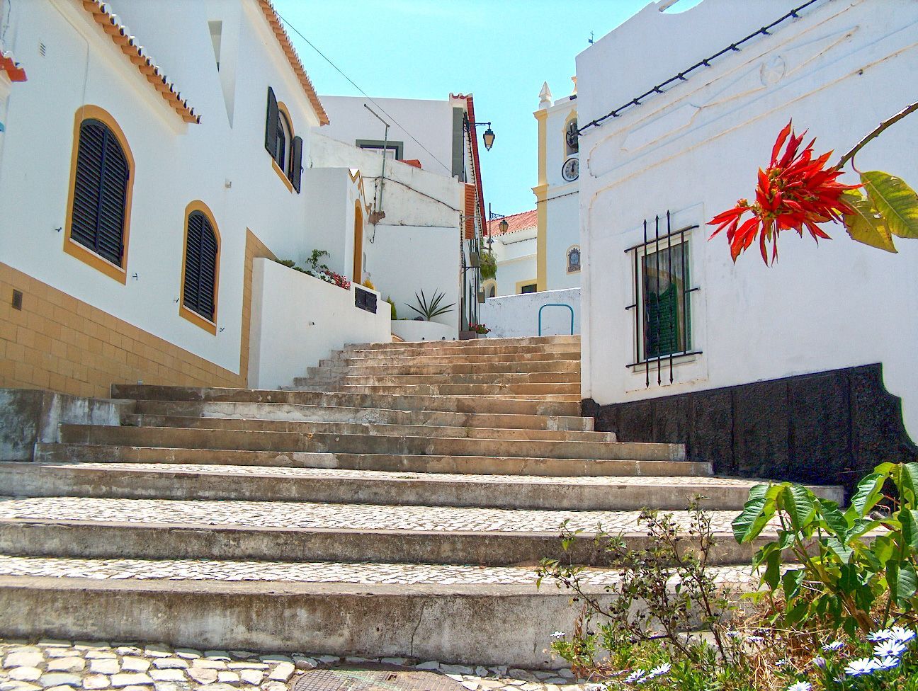 Stairway in white-washed town, Portugal; flowers on building, leading to church in the distance.