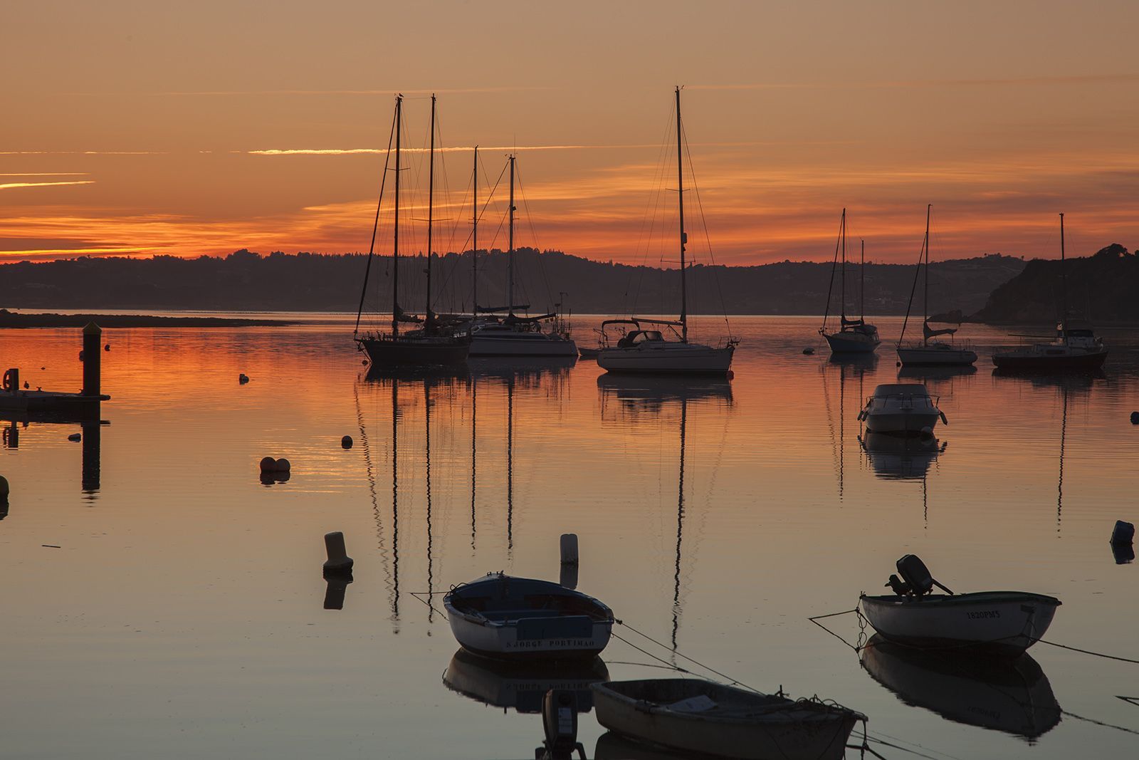 Boats moored in calm water at sunset, with masts reflecting in the golden light.