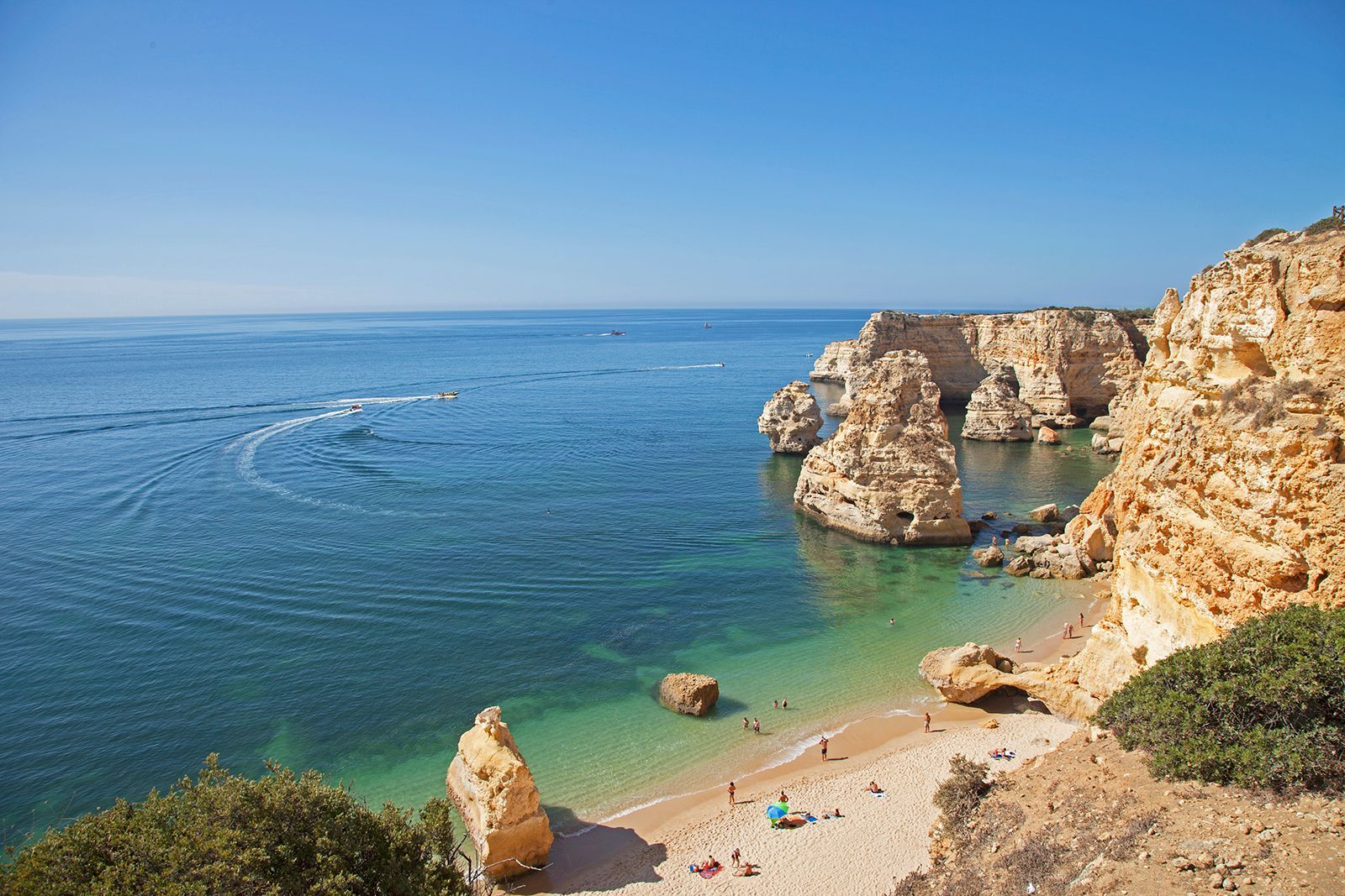 Coastal view of a clear blue ocean, sandy beach, and tan cliffs under a clear sky.