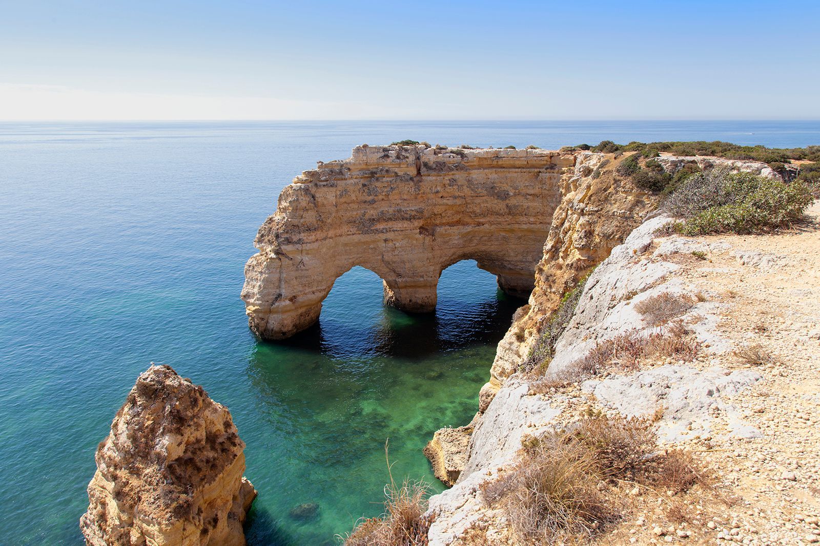 Cliffs with two natural archways over turquoise water under a clear blue sky.