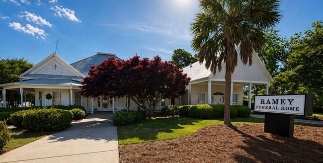 Tree-lined office building with pink flowering crepe myrtles beside a driveway and sign.
