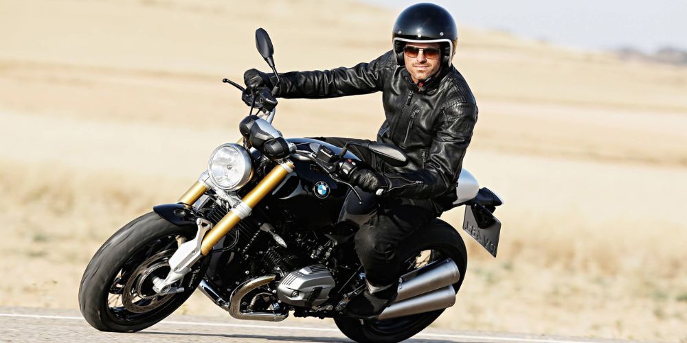 A man is riding a BMW R NineT down a road.