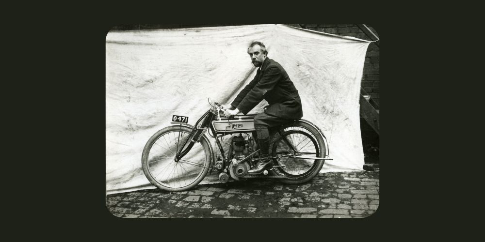 James Lansdowne Norton is riding a motorcycle on a cobblestone street.