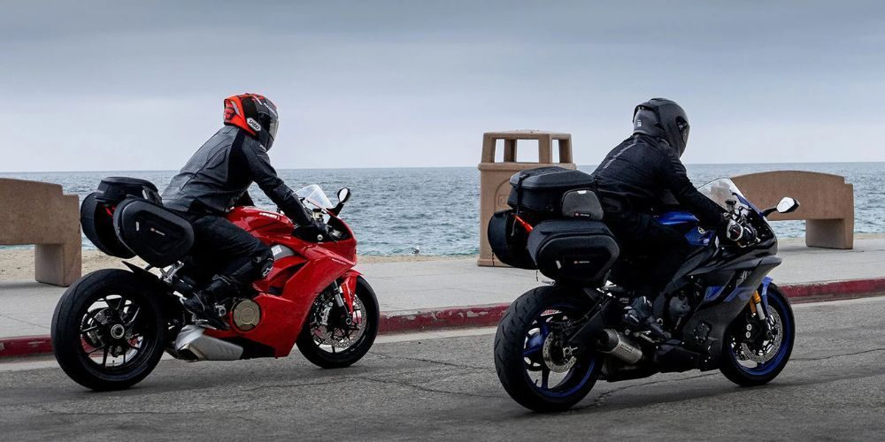 Two people are riding motorcycles down a street next to the ocean.