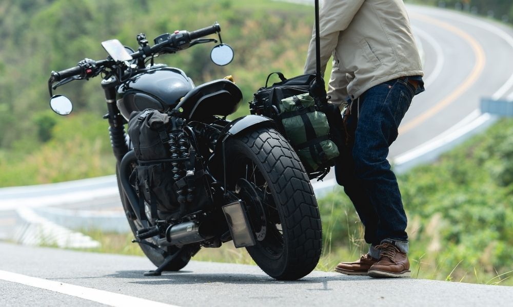A man is standing next to a motorcycle on the side of a road.