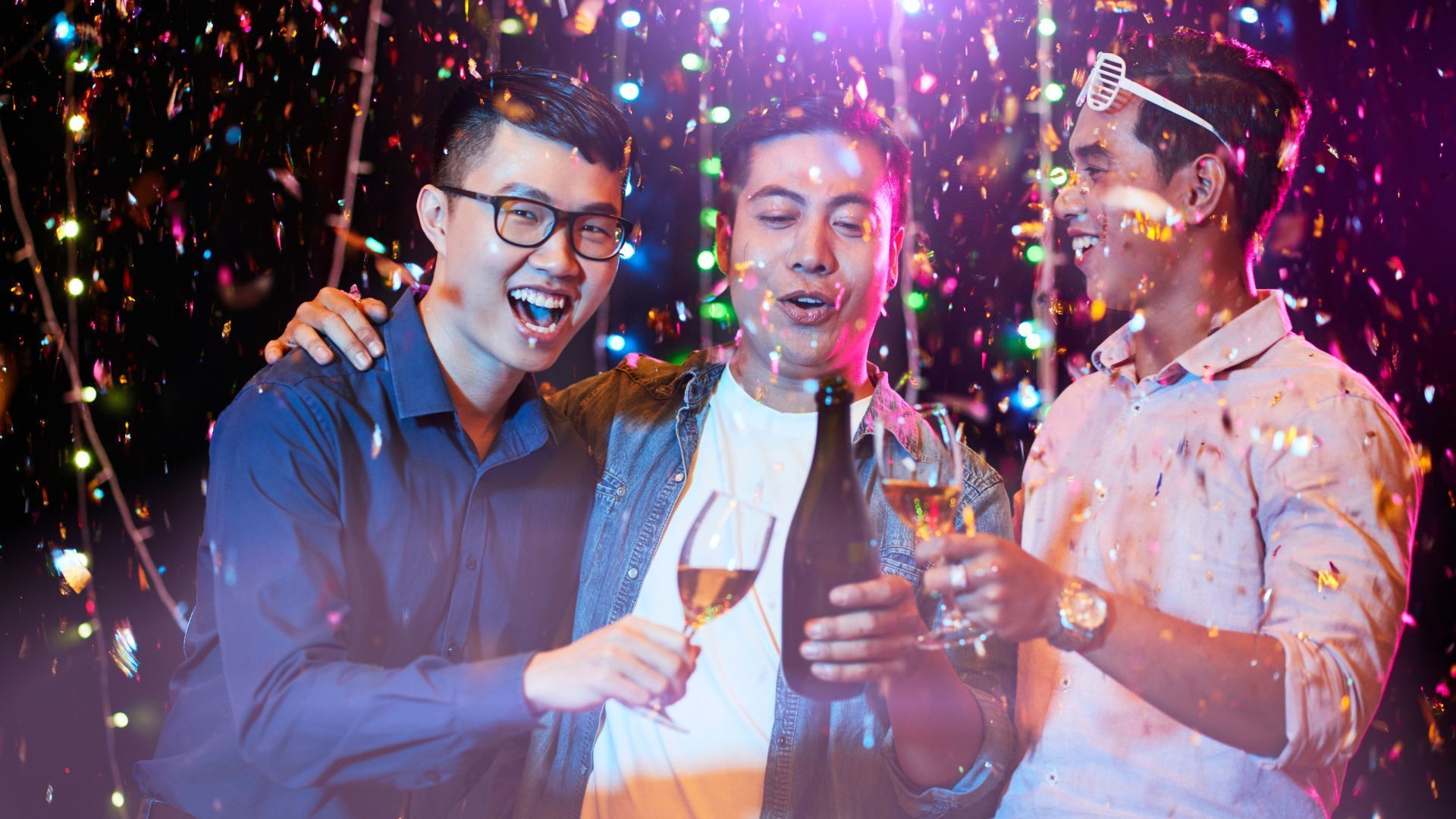 Three men are toasting with champagne and confetti at a party.