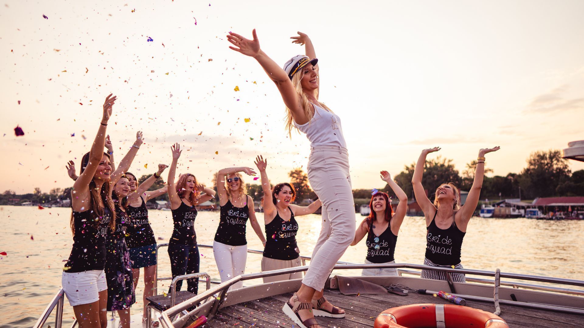 A group of women are standing on a boat throwing confetti