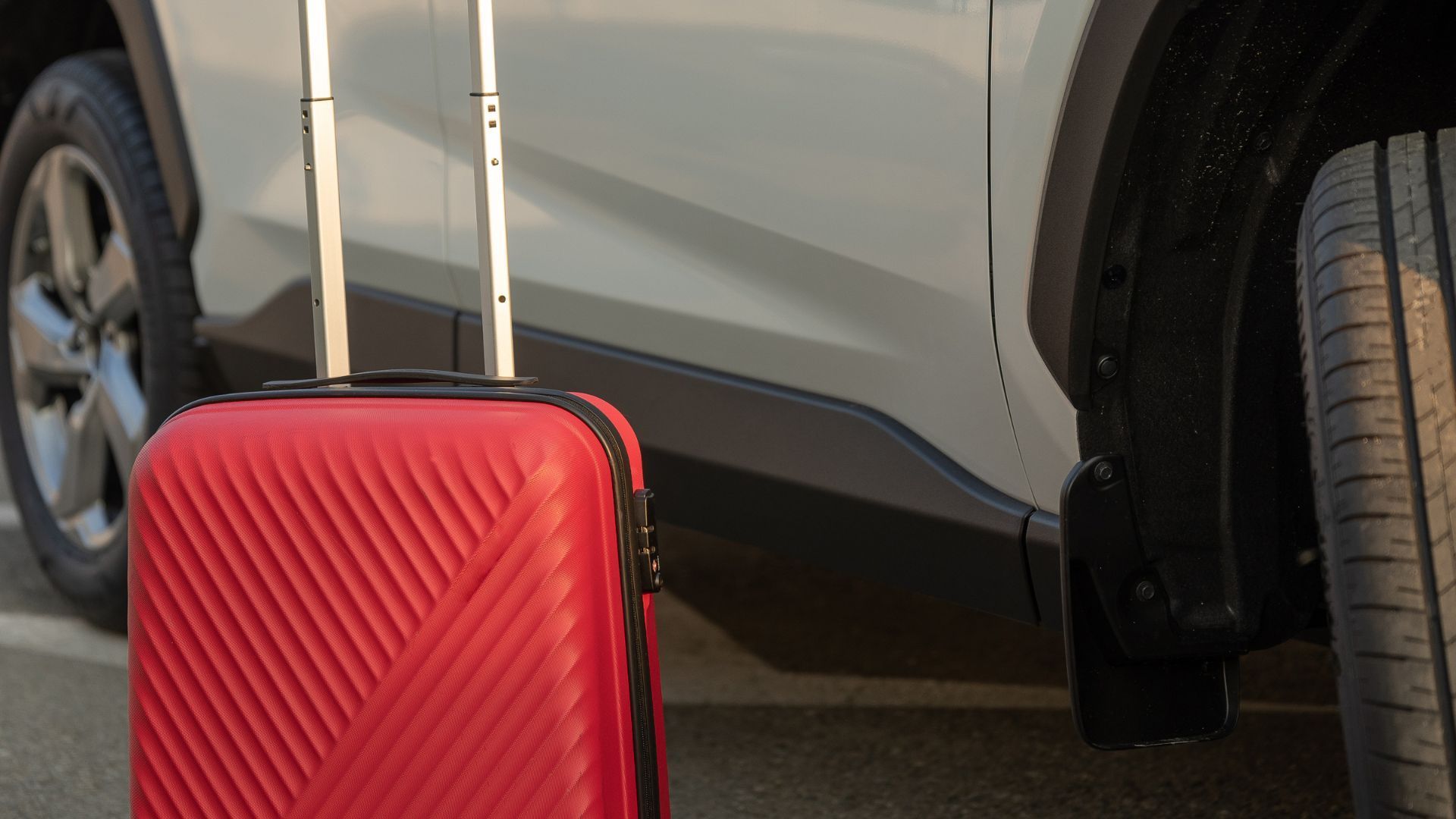 A red suitcase is sitting next to a white car