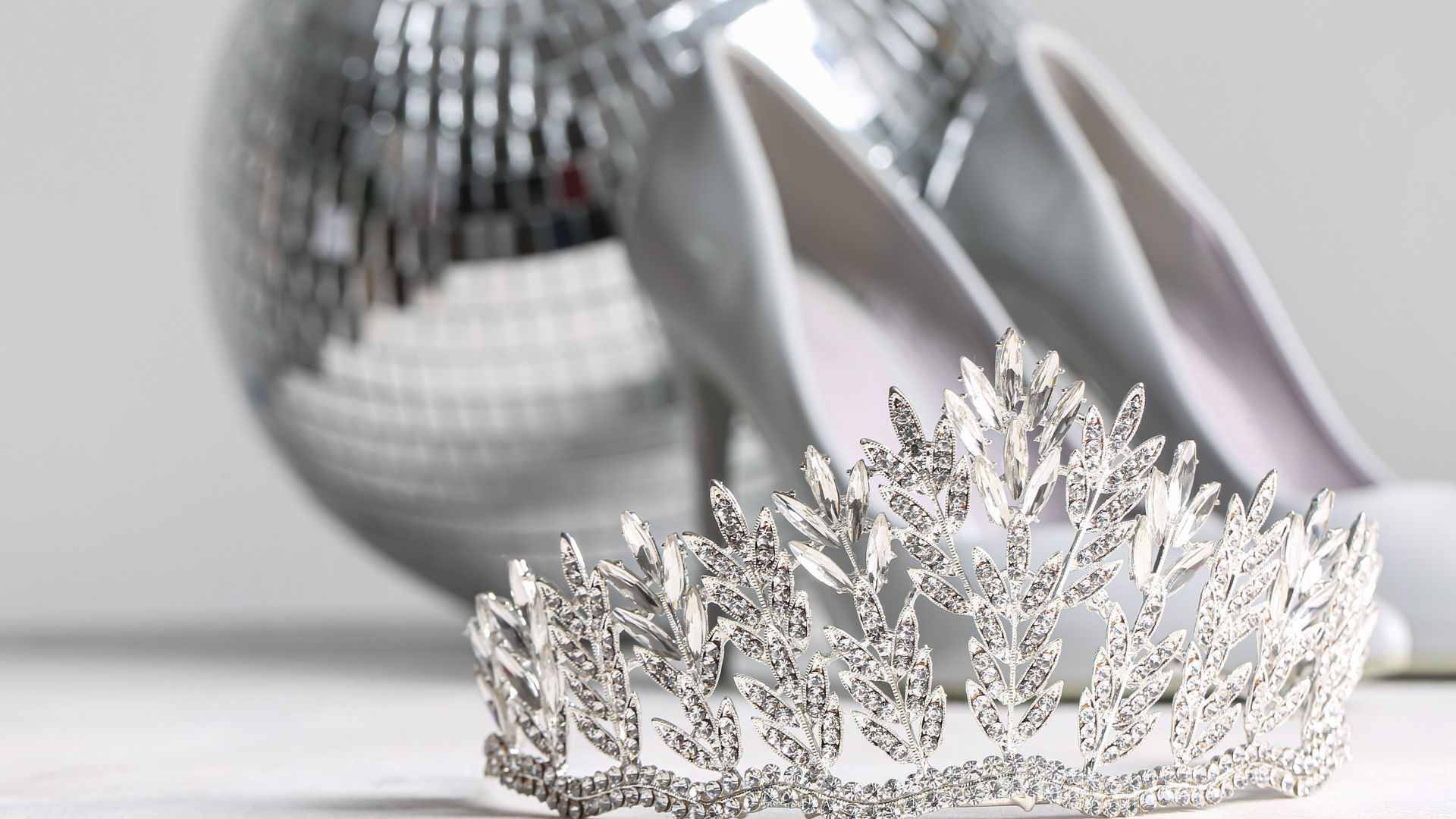 A pair of silver shoes and a tiara are on a table.