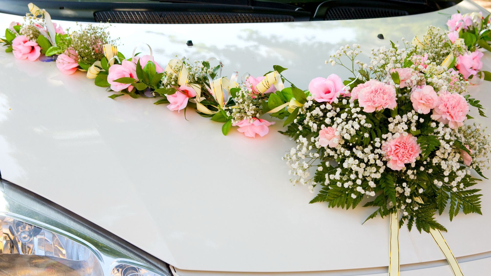 A white car is decorated with pink and white flowers