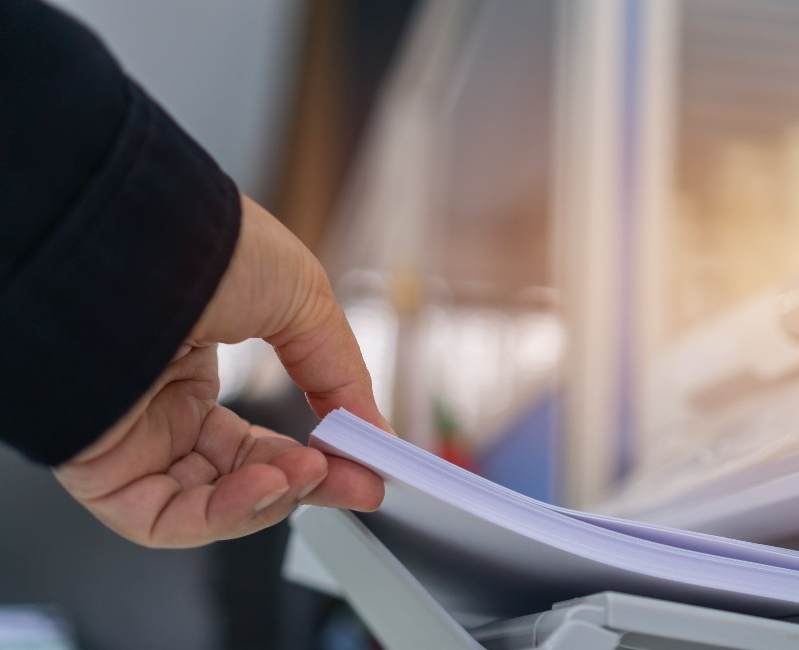 A person is utilizing document solutions to take paper from a printer.