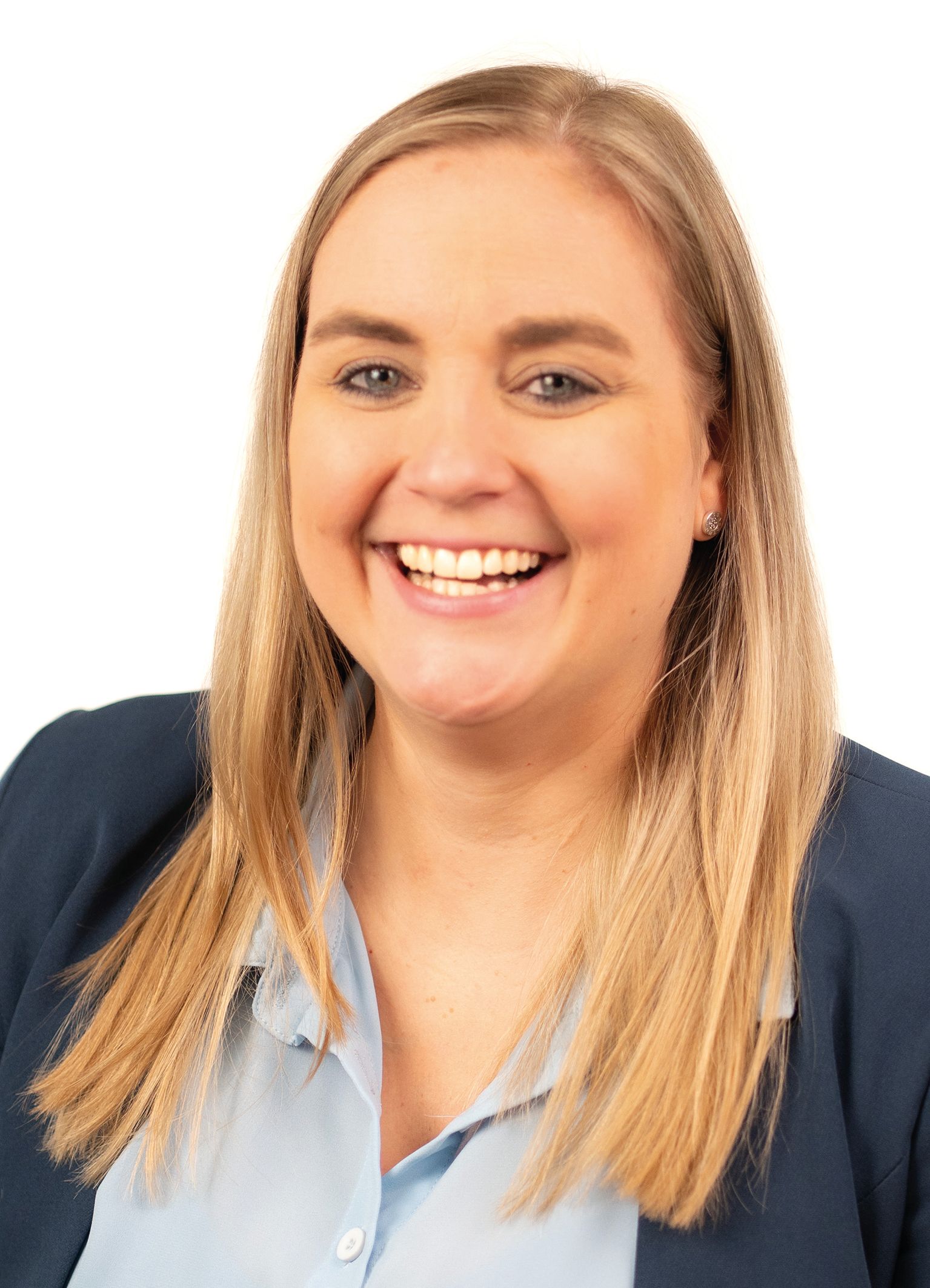 Blonde Frau lächelt, trägt ein blaues Hemd und einen Blazer, vor weißem Hintergrund.