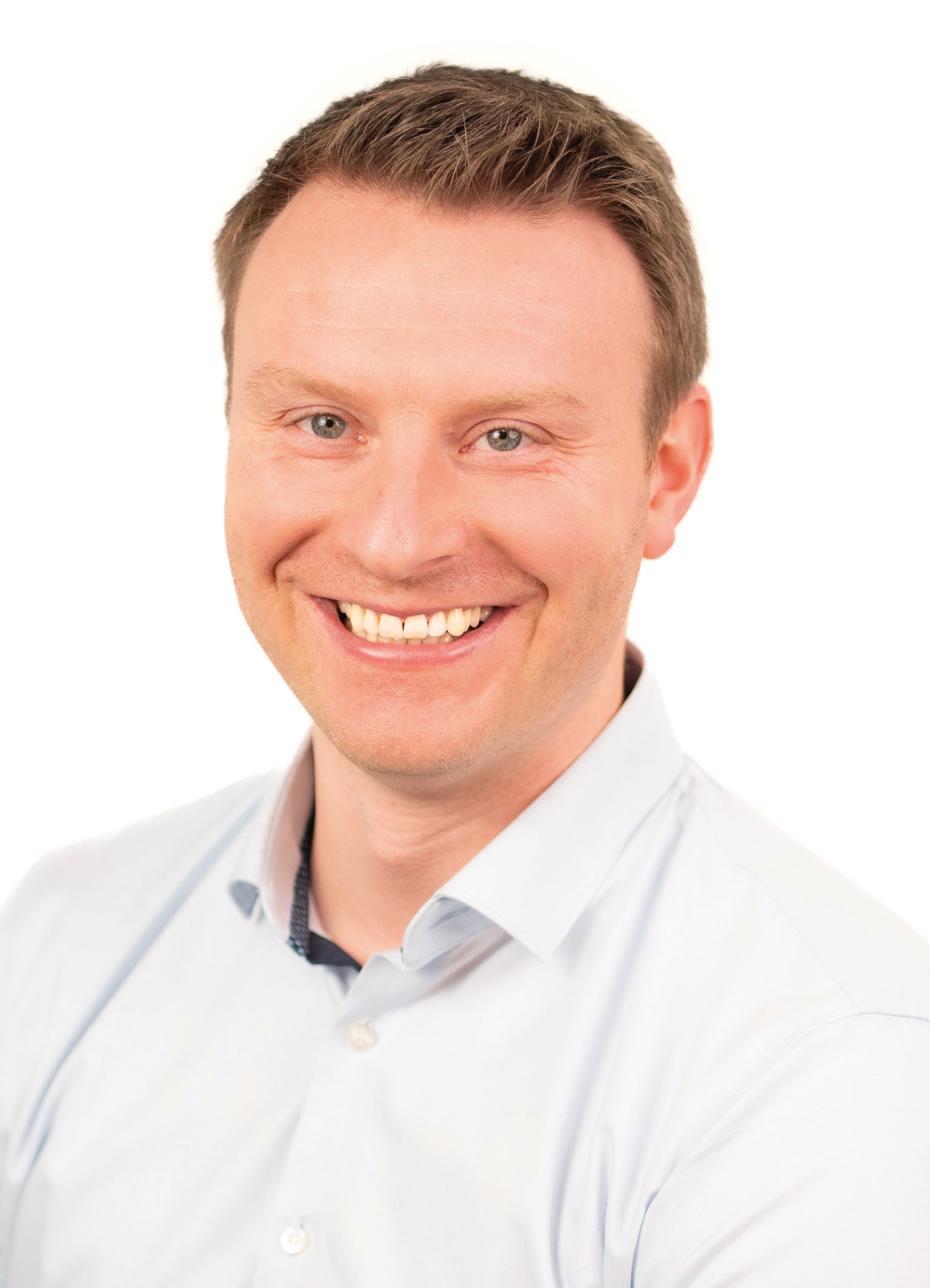 Lächelnder Mann in hellblauem Hemd vor weißem Hintergrund.