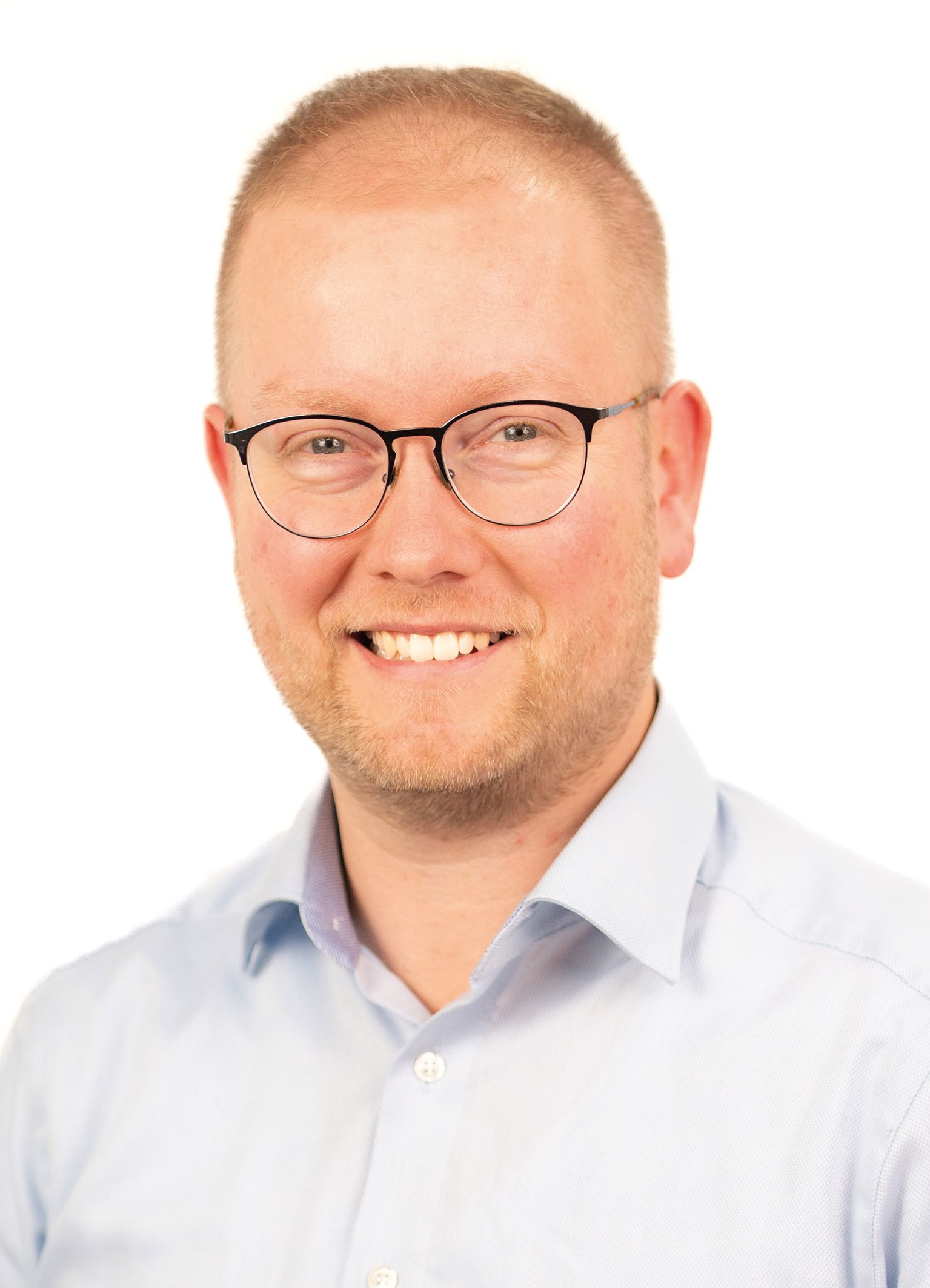 Mann mit Brille lächelt, hellblaues Hemd, vor weißem Hintergrund.