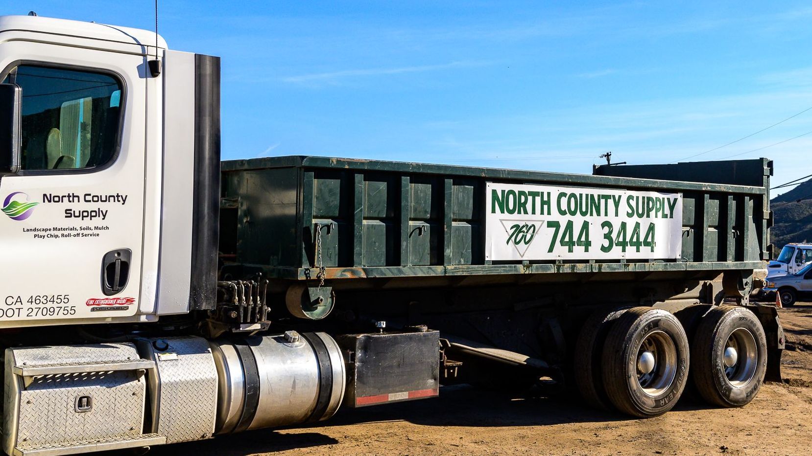 A north county dump truck is parked in a dirt lot