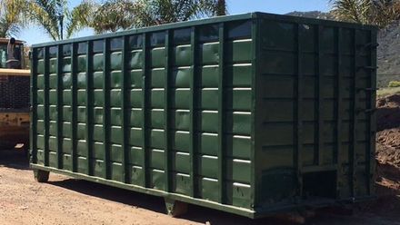 A large green dumpster is parked on the side of the road next to a bulldozer.